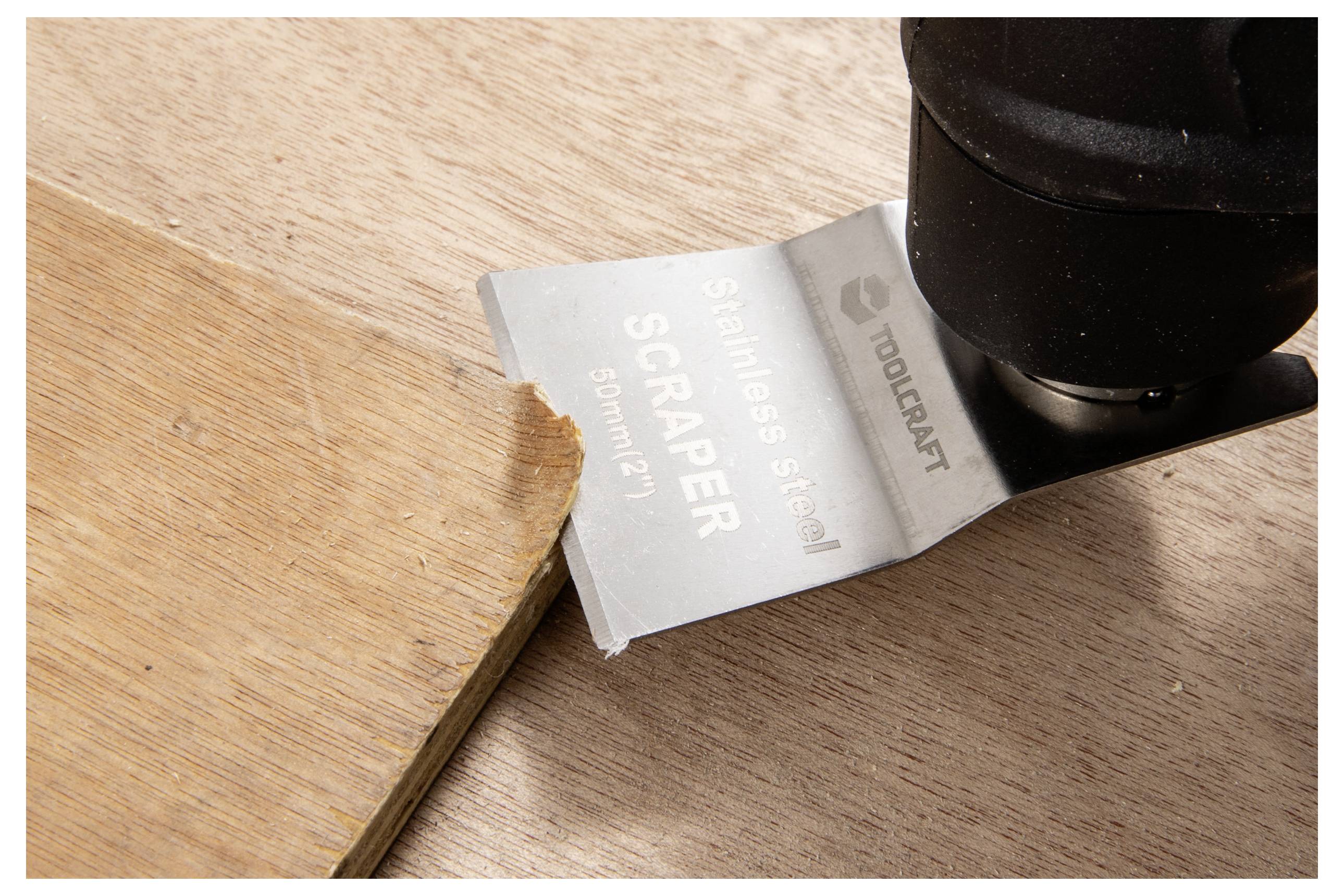 Eine Nahaufnahme eines Schabwerkzeugs, das eine Holzkante abträgt, mit einem Metallblatt, das mit dem Text „Edelstahl-Schaber