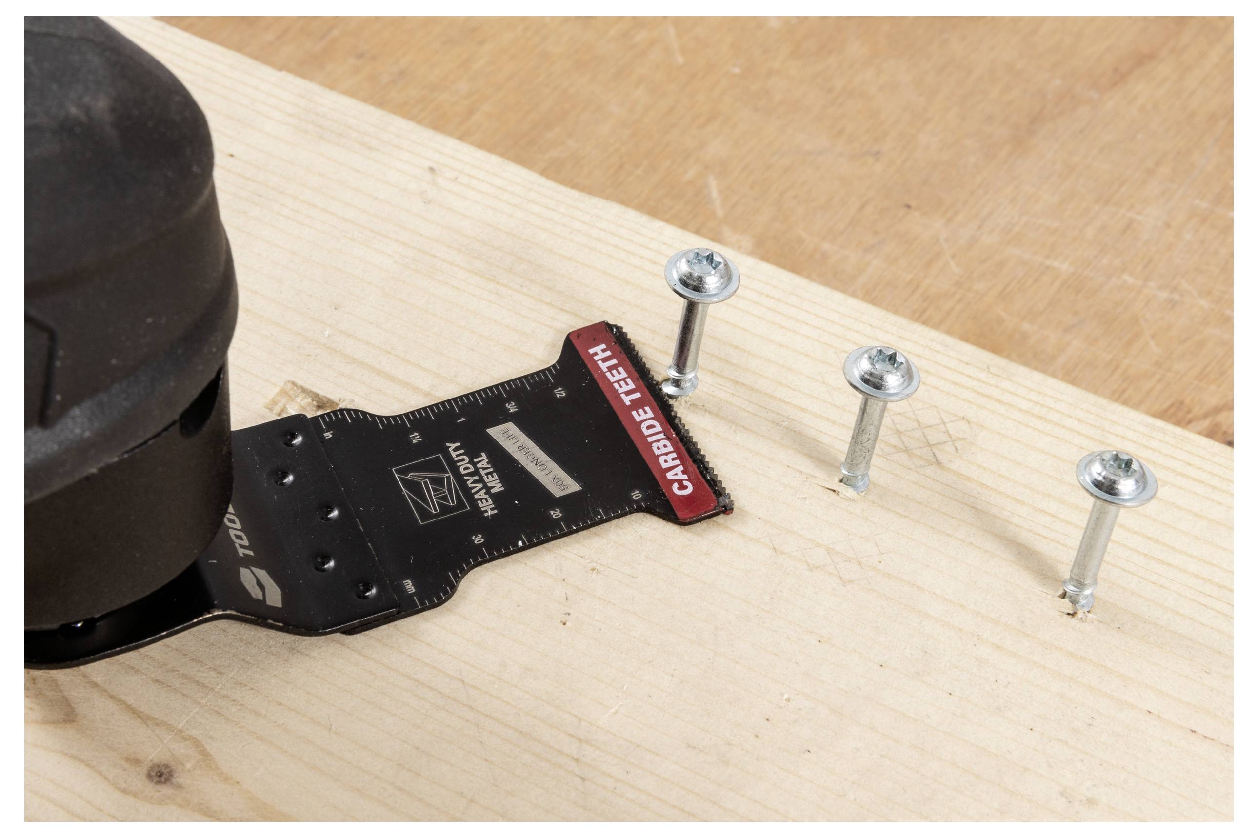 Eine elektrische Säge, die durch Holz schneidet, neben drei teilweise eingedrehten Schrauben. Die Sägeblatt ist mit „Hartmetallzähnen