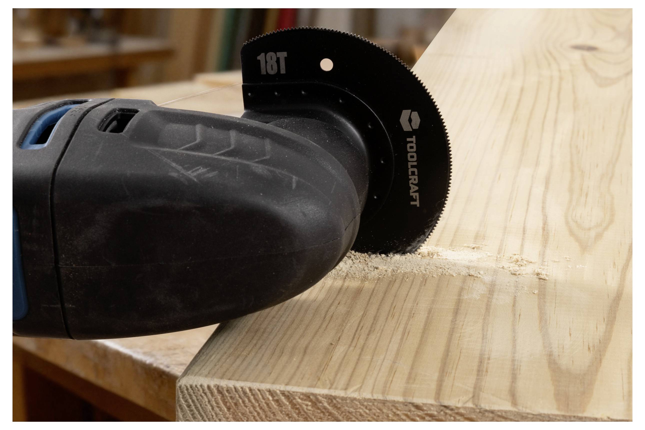 Ein Elektrowerkzeug mit einer Sägeblatt arbeitet an einem Holzbrett und erzeugt Sägespäne. Das Blatt zeigt '18T' und 'Toolcraft.'