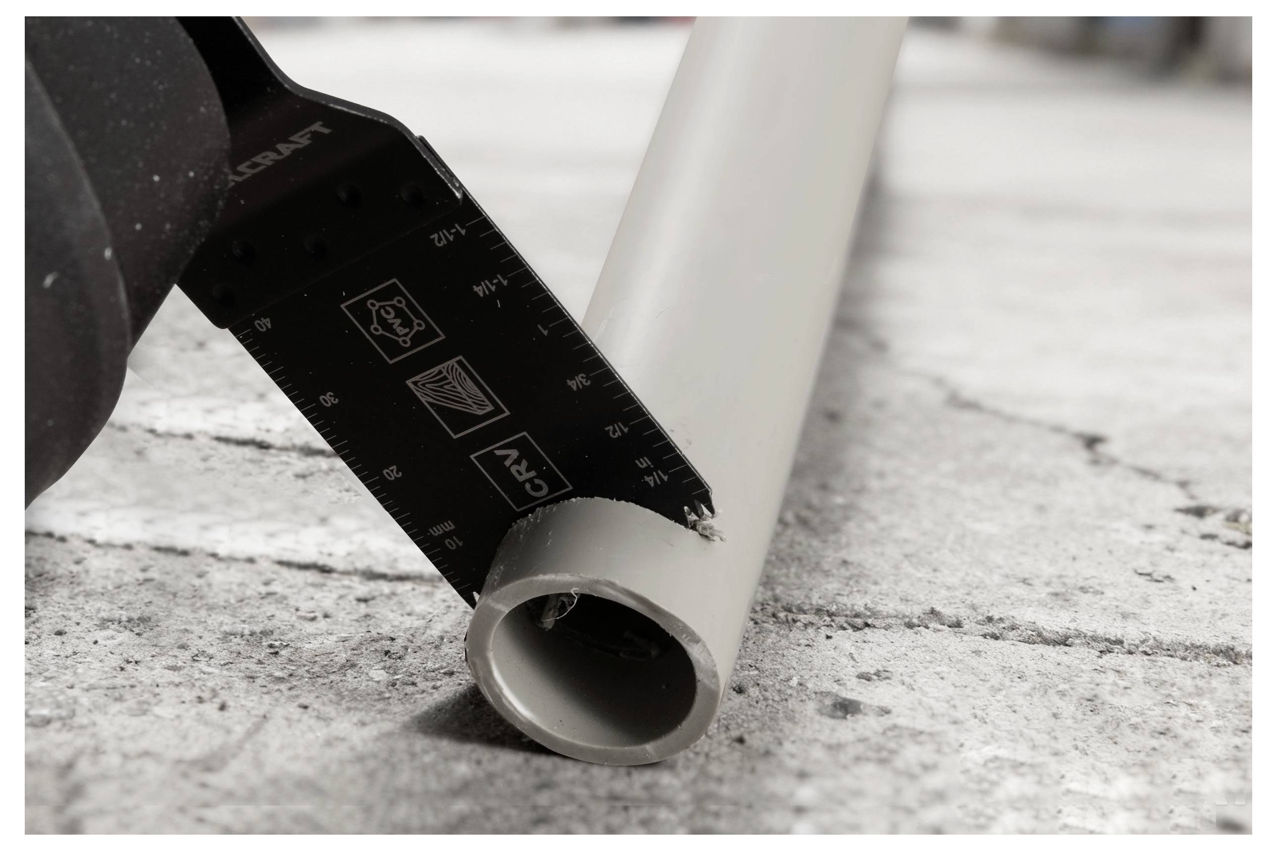 Ein Utility-Messer, das ein graues PVC-Rohr auf einer Betonoberfläche durchschneidet, teilweise durch das Rohr mit sichtbaren Schnittmarkierungen.