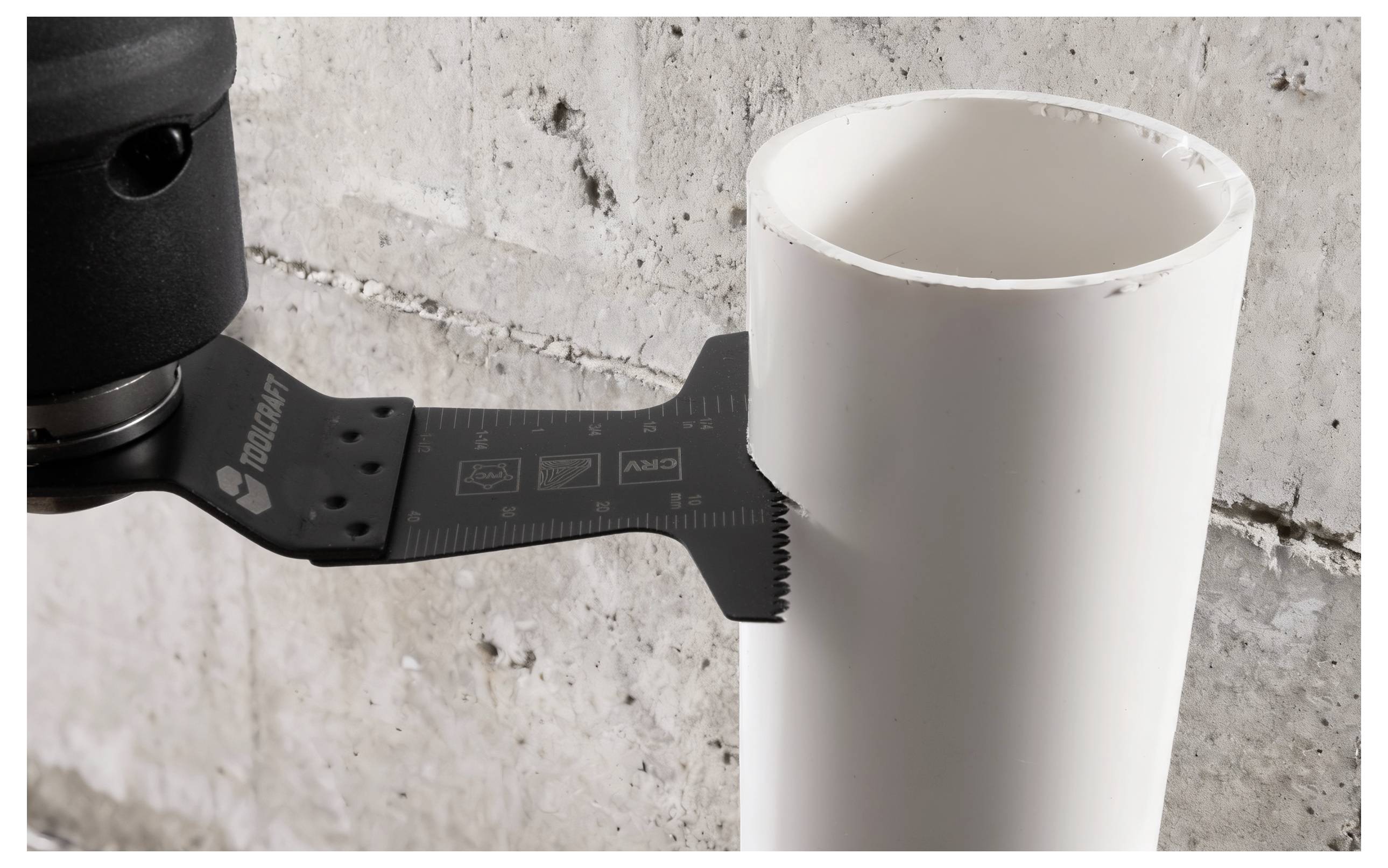 Ein Werkzeug schneidet in ein weißes PVC-Rohr an einer Betonwand und demonstriert dabei seine Funktion für präzise Rohrarbeiten.