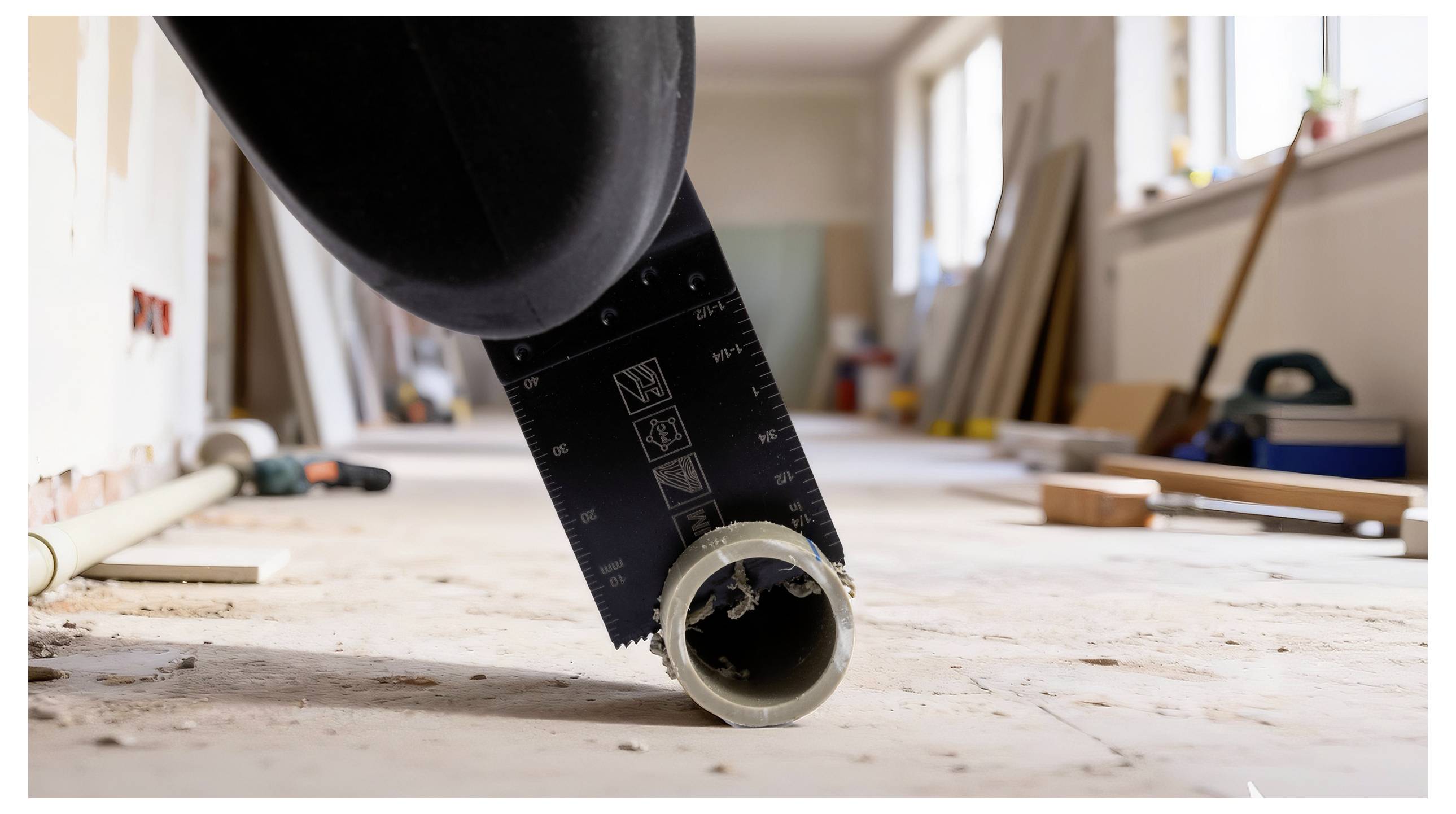 Eine Sägeblatt schneidet durch ein Kunststoffrohr auf dem Boden einer Baustelle mit Werkzeugen und Materialien im Hintergrund.