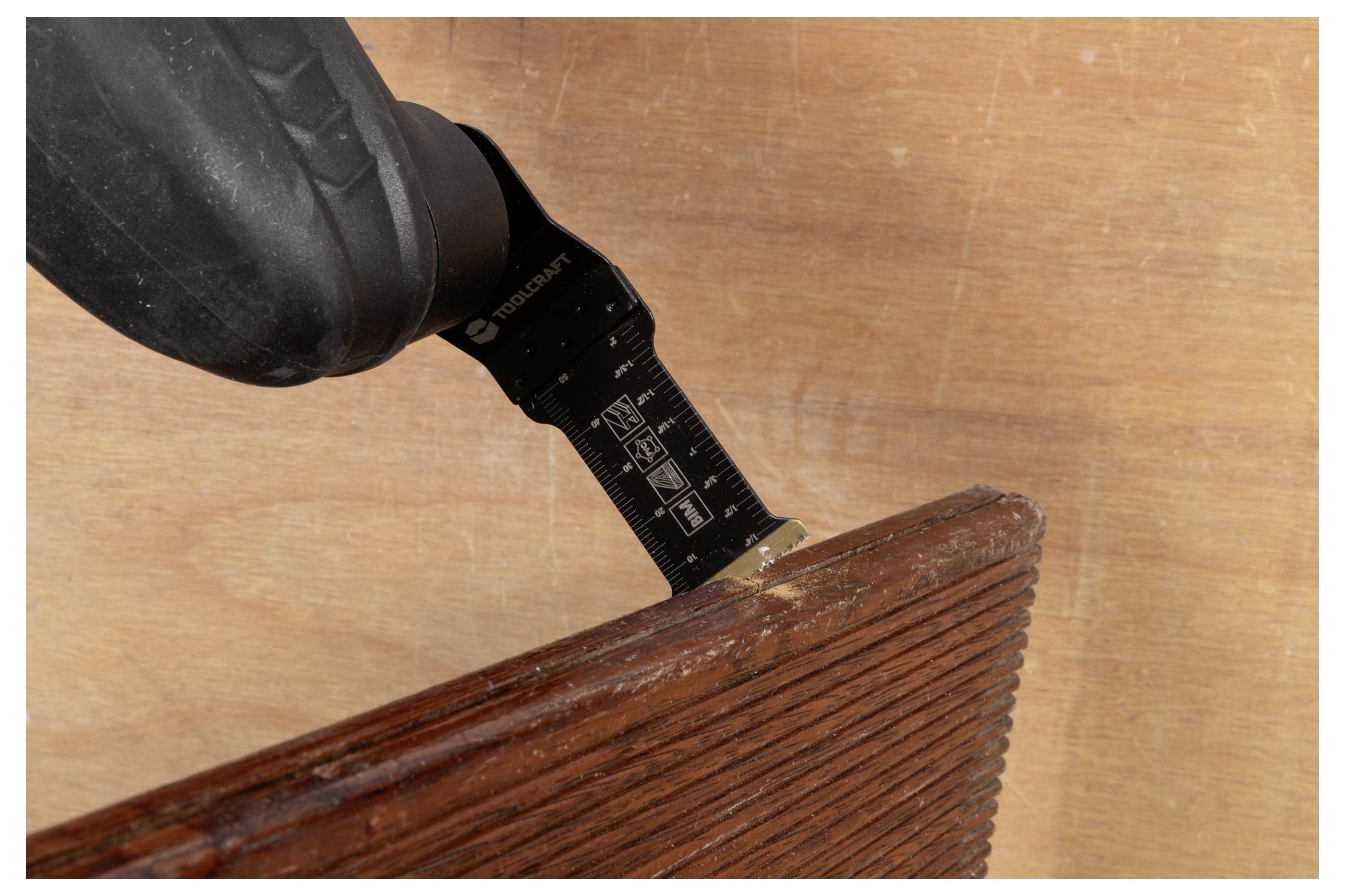 Eine Elektrowerkzeug mit einer oszillierenden Klinge schneidet ein Stück Holz mit einer strukturierten Oberfläche.