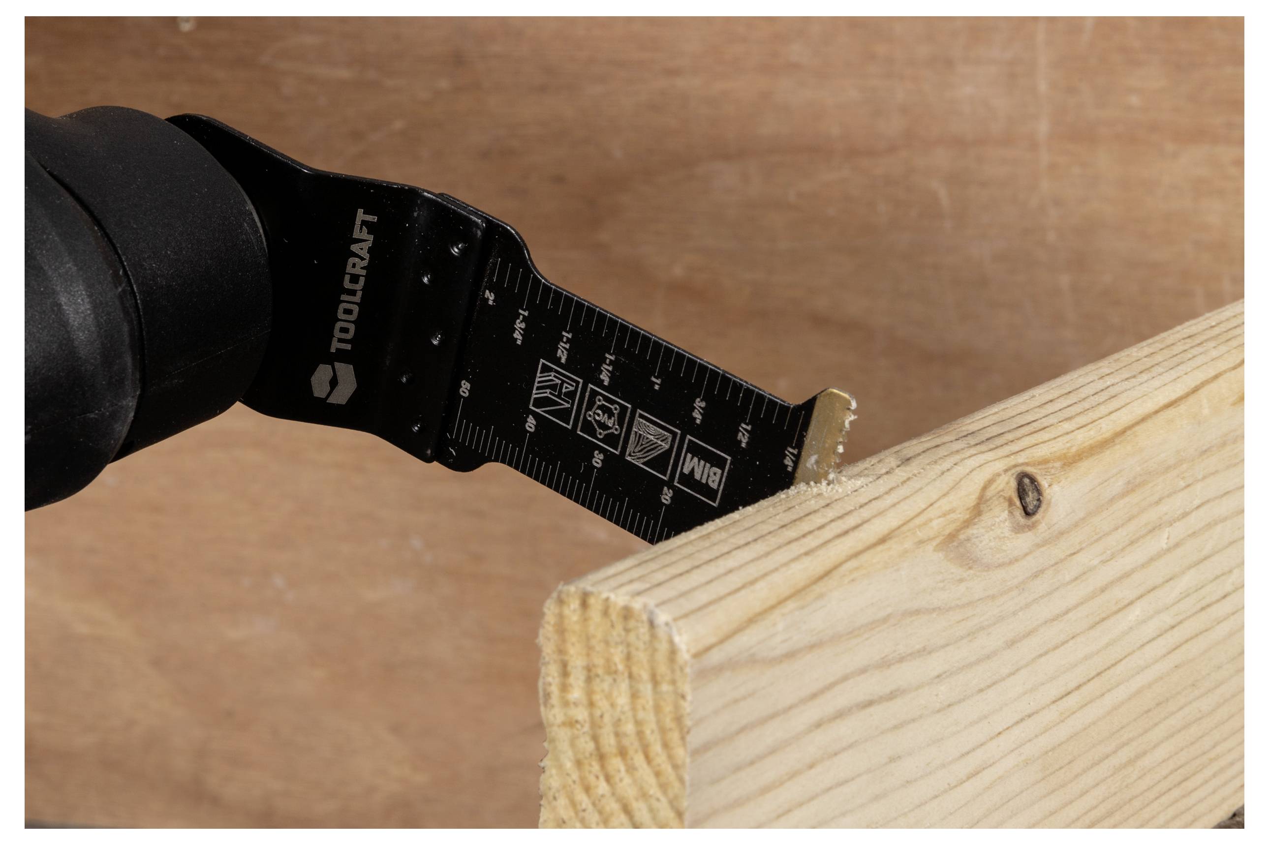 Eine Nahaufnahme eines tragbaren Oszillationswerkzeugs mit einer Sägeblatt, das durch ein Holzbrett schneidet und dabei Details der Holzstruktur und Maßstabsmarkierungen des Werkzeugs zeigt.