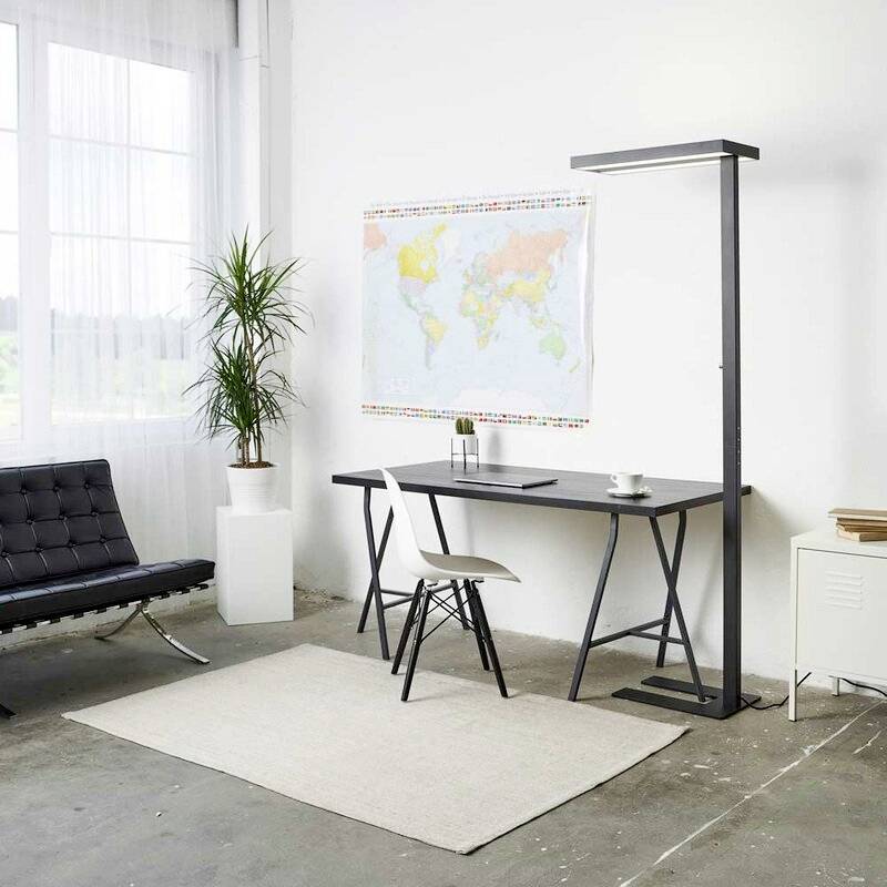 Ein minimalistisches Büro mit modernem Schreibtisch, Stuhl, Stehlampe, Pflanze und Weltkarte an der Wand. Fenster lässt Tageslicht herein.