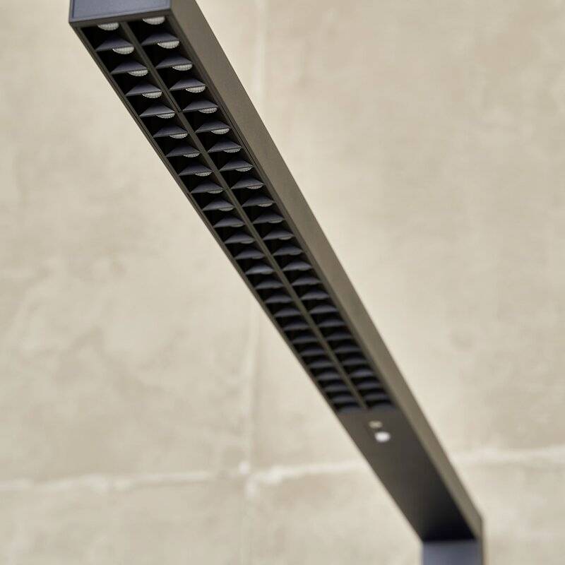 Eine dunkle, längliche Lampe mit quadratischen Lichtöffnungen, die an einem beigen Hintergrund positioniert ist.