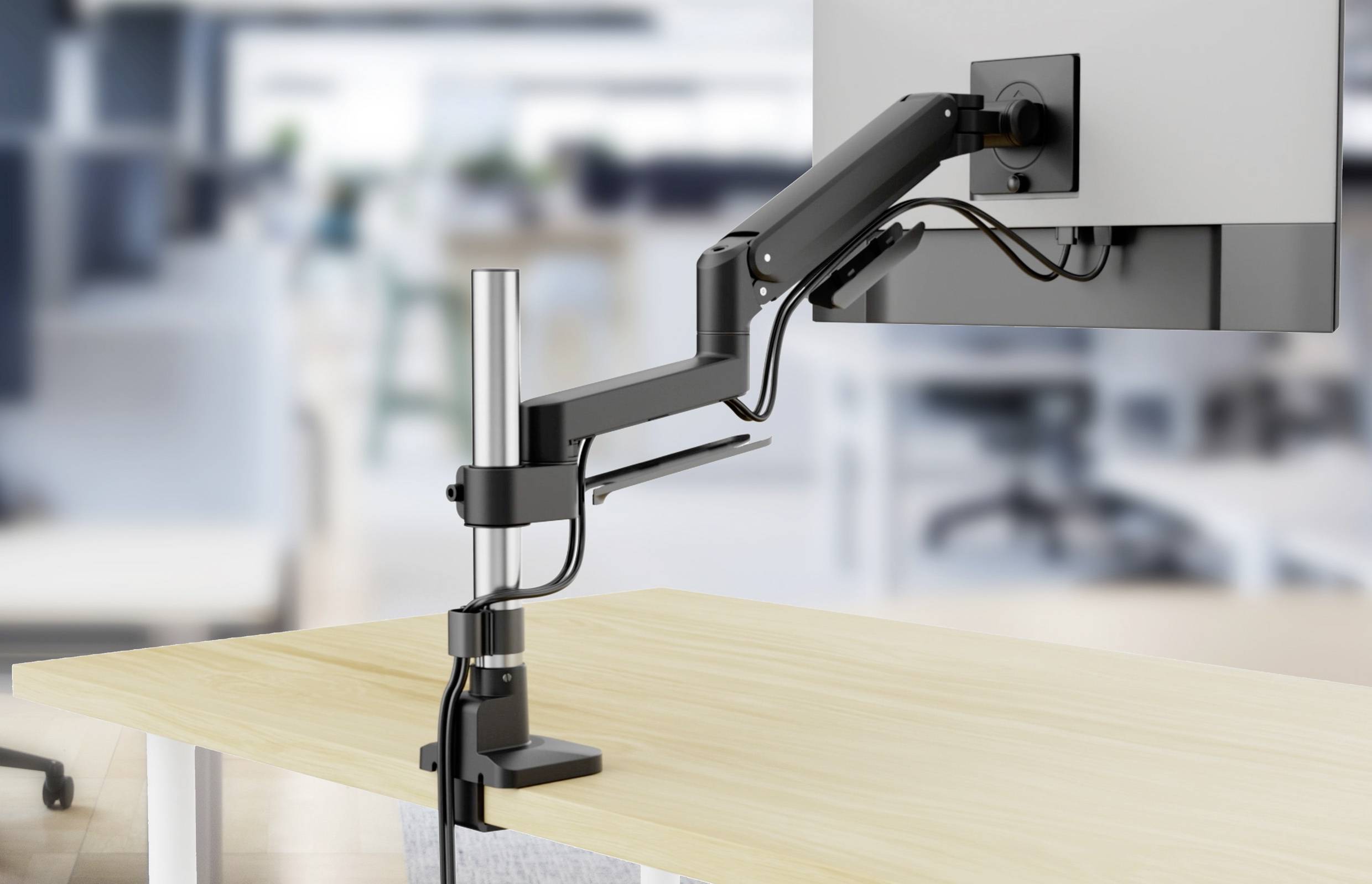 Ein Monitor mit verstellbarem Arm ist auf einem Büroschreibtisch montiert. Der Hintergrund zeigt eine unscharf gehaltene Büroumgebung als Kontextgeber.