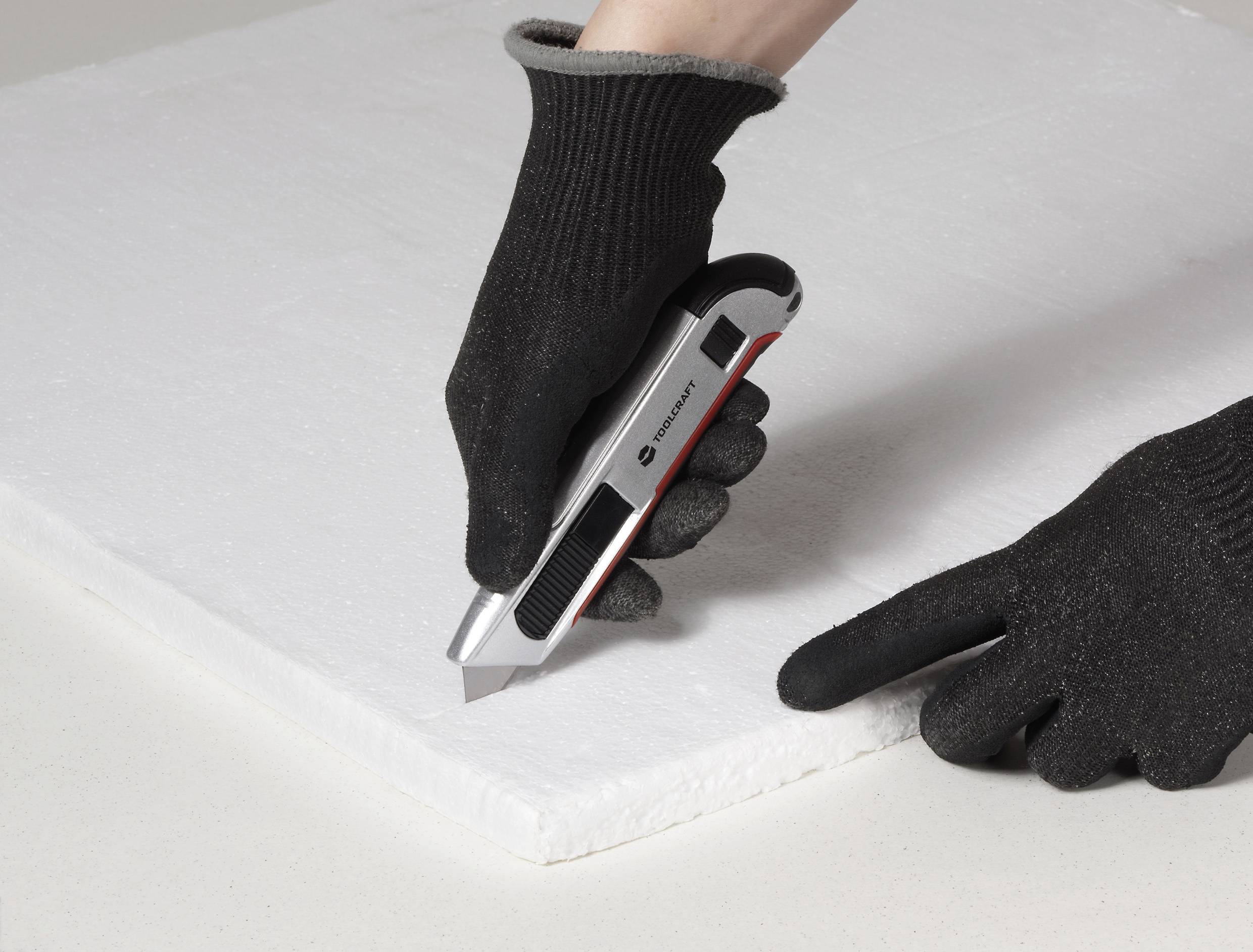 Eine Hand mit Handschuh, die ein Utility-Messer verwendet, um ein weißes Schaumstoffstück auf einer flachen Oberfläche zu schneiden und dabei einen DIY-Projekt oder eine Bastelaufgabe zu veranschaulichen.