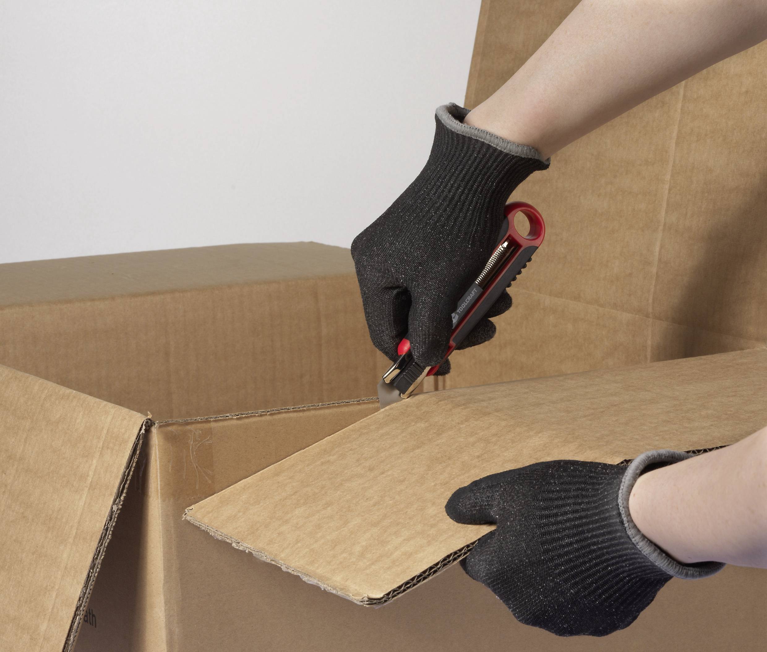 Hände in schwarzen Handschuhen, die ein Utility-Messer halten und vorsichtig einen großen Karton aufschneiden.