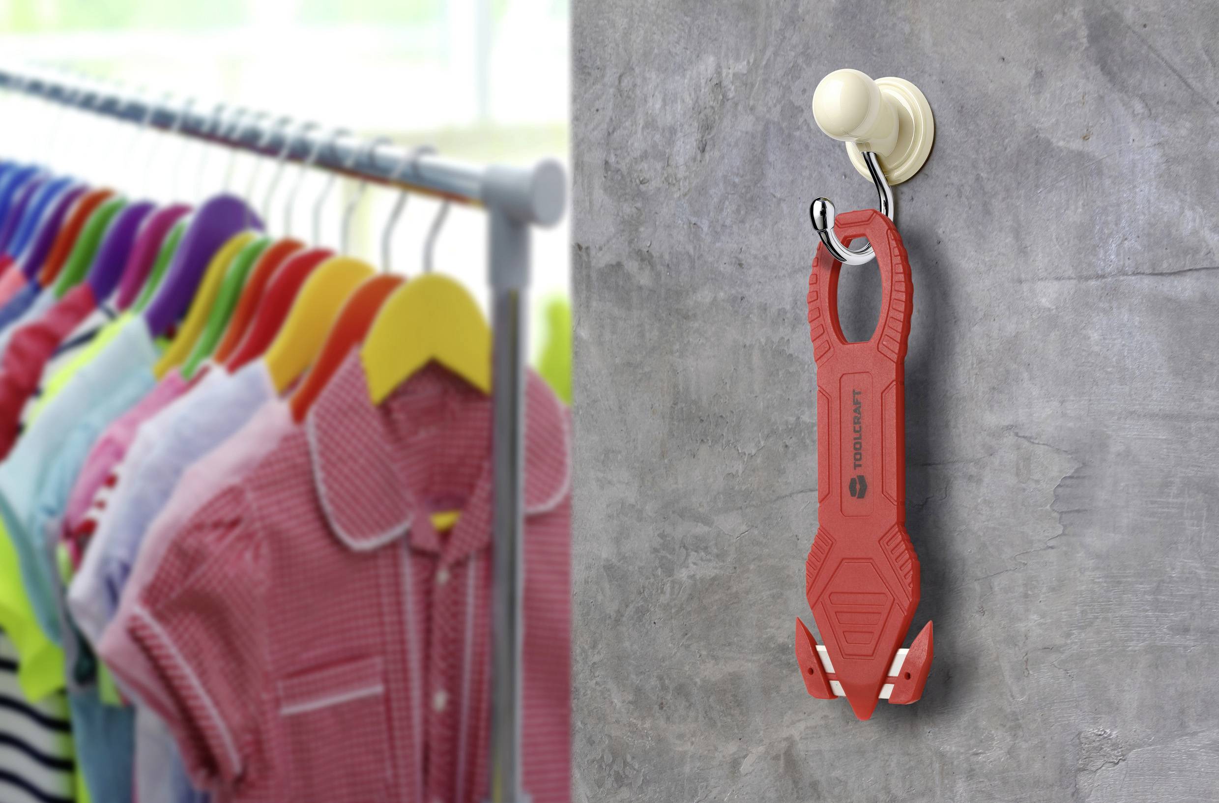 Ein rotes Multitool hängt an einem Wandhaken neben einem Ständer mit bunten Kleidungsstücken auf Kleiderbügeln. Das Werkzeug ist mit 'FIDLOCK' gekennzeichnet.