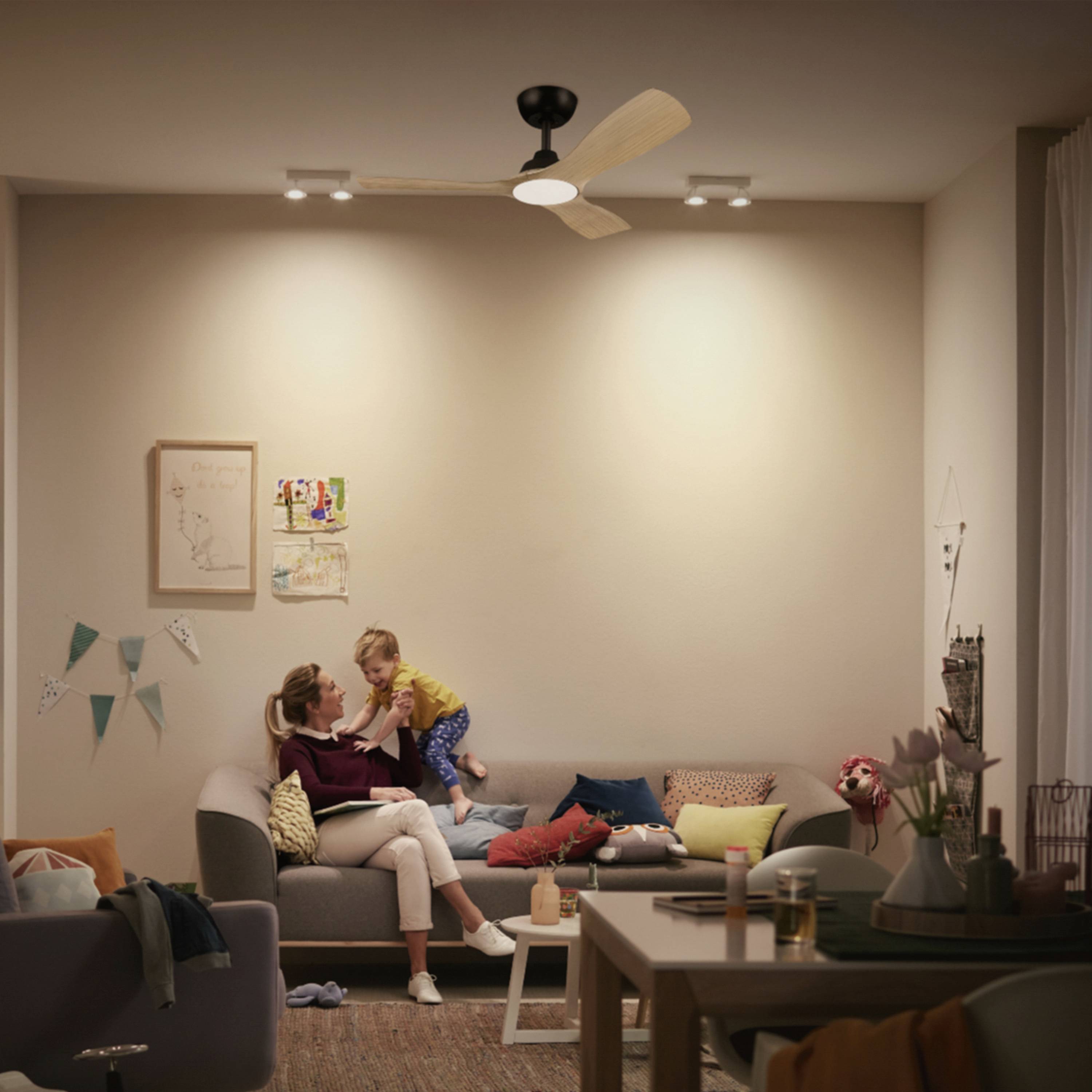 Eine Frau sitzt auf einem Sofa und hält ein lächelndes Kind. Das Wohnzimmer ist gemütlich mit Dekorationen und warmem Licht.