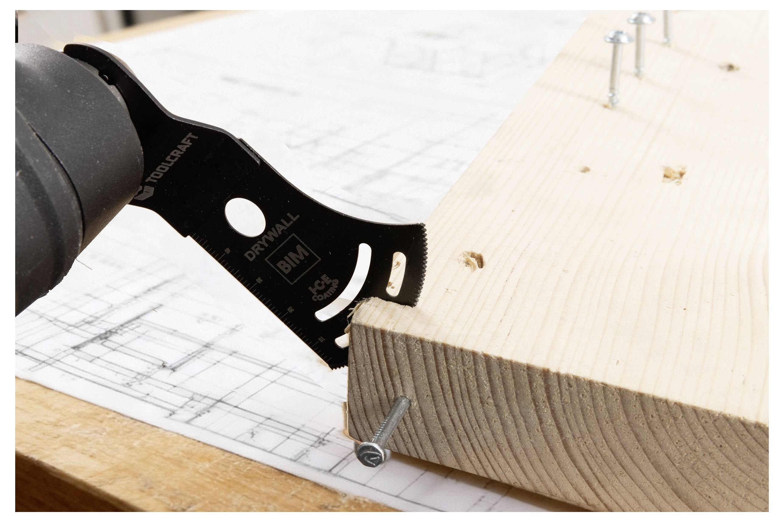 Eine Elektrowerkzeug mit einer Schneidklinge beschneidet den Rand eines Holzbretts, das über einem Bauplan liegt. Schrauben sind teilweise in das Brett eingedreht.