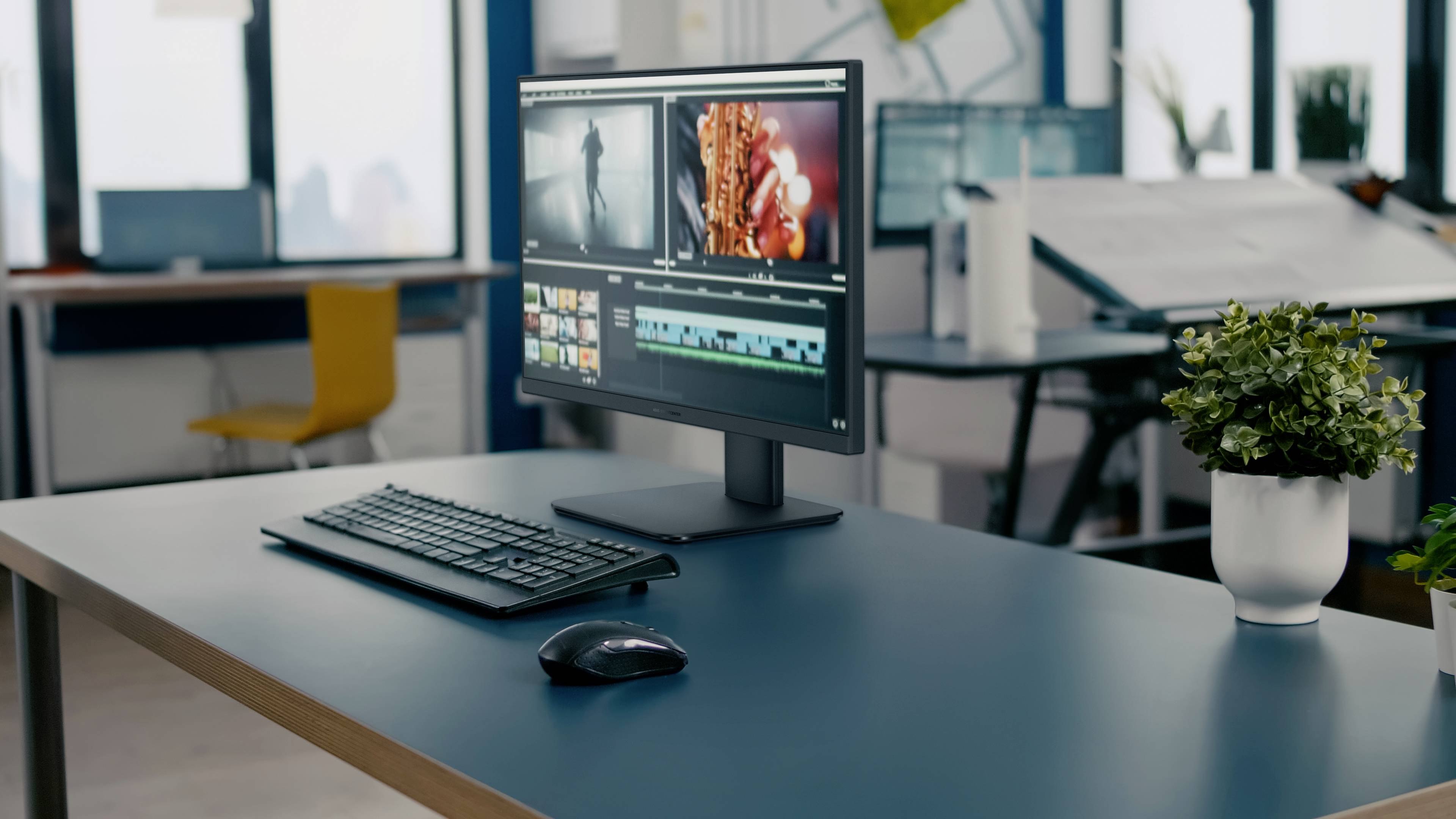 Ein Computermonitor auf einem Schreibtisch zeigt eine Videobearbeitungssoftware-Oberfläche, begleitet von einer Tastatur und einer Maus. Eine Topfpflanze befindet sich in der Nähe.