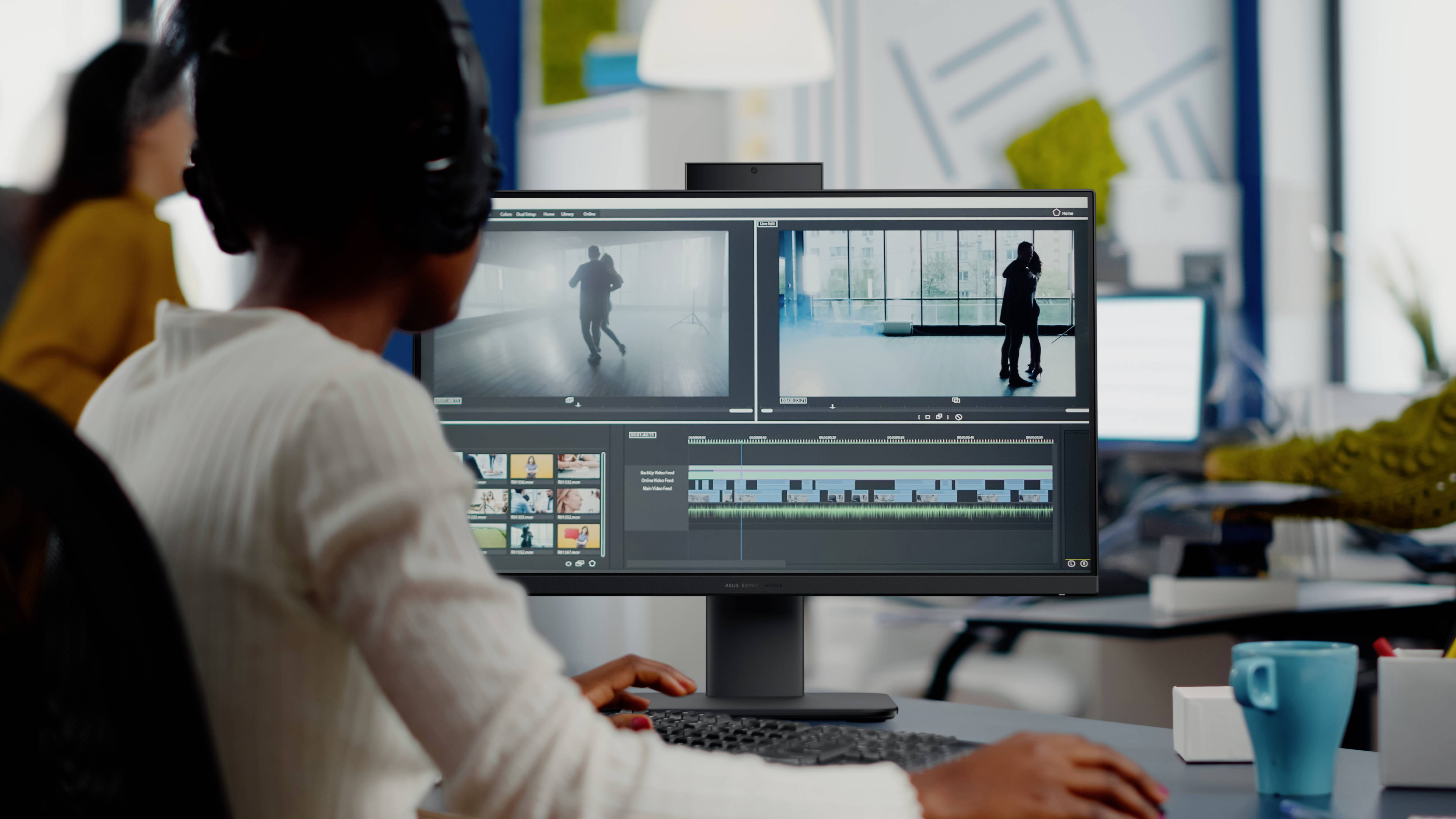 Eine Person mit Kopfhörern bearbeitet Videomaterial an einem Computer in einem Büroumfeld. Der Bildschirm zeigt eine Zeitleiste und Vorschau-Clips.