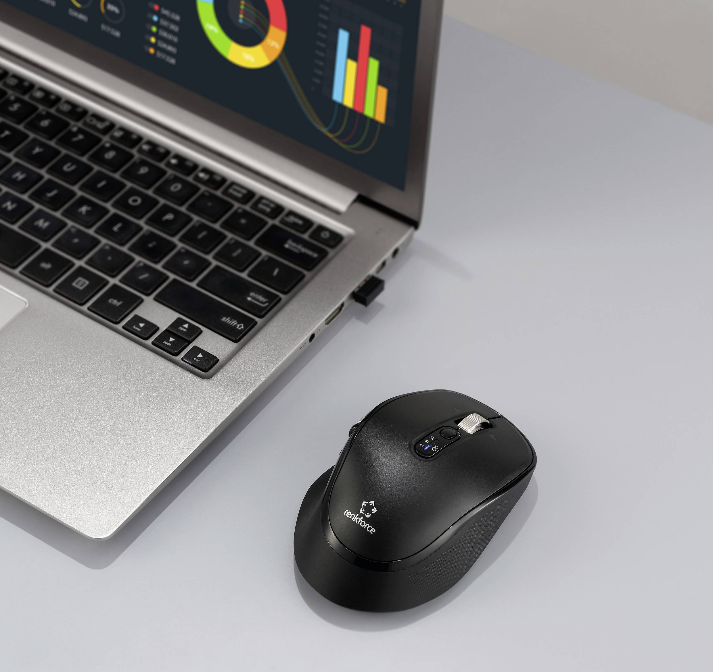 Ein Laptop, der bunte Grafiken zeigt, neben einer drahtlosen Maus auf einer grauen Oberfläche.