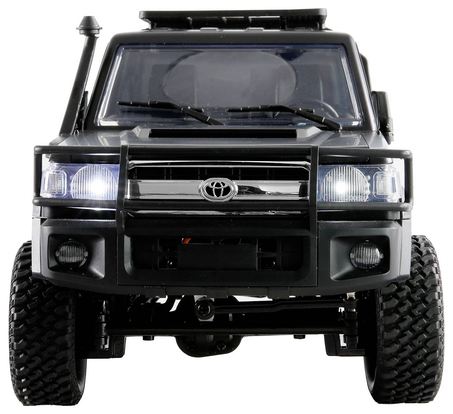 Vorderansicht eines schwarzen Geländewagens mit bulligem Kühlergrill und eingeschalteten Scheinwerfern, auf unbefestigtem Gelände.