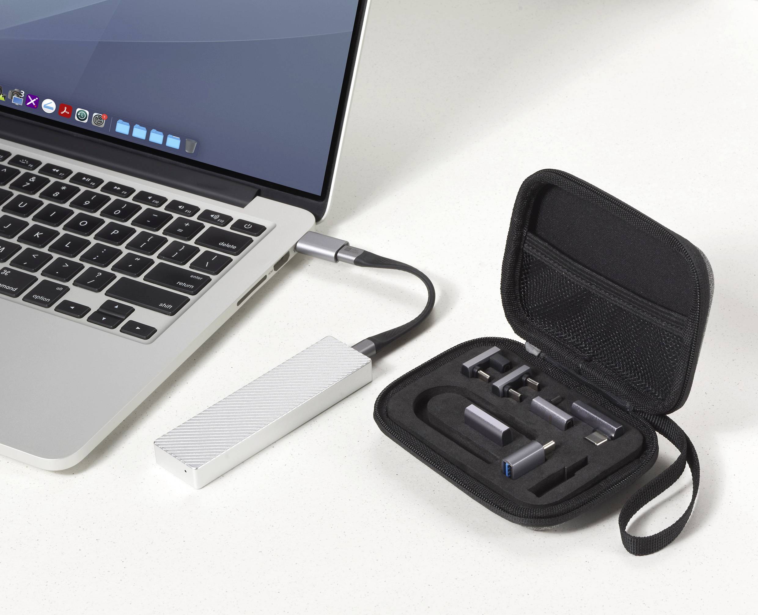 Ein Laptop auf einem Schreibtisch ist mit einer tragbaren externen SSD verbunden. Daneben zeigt ein geöffnetes Gehäuse mehrere USB-Anschlüsse und Adapter.