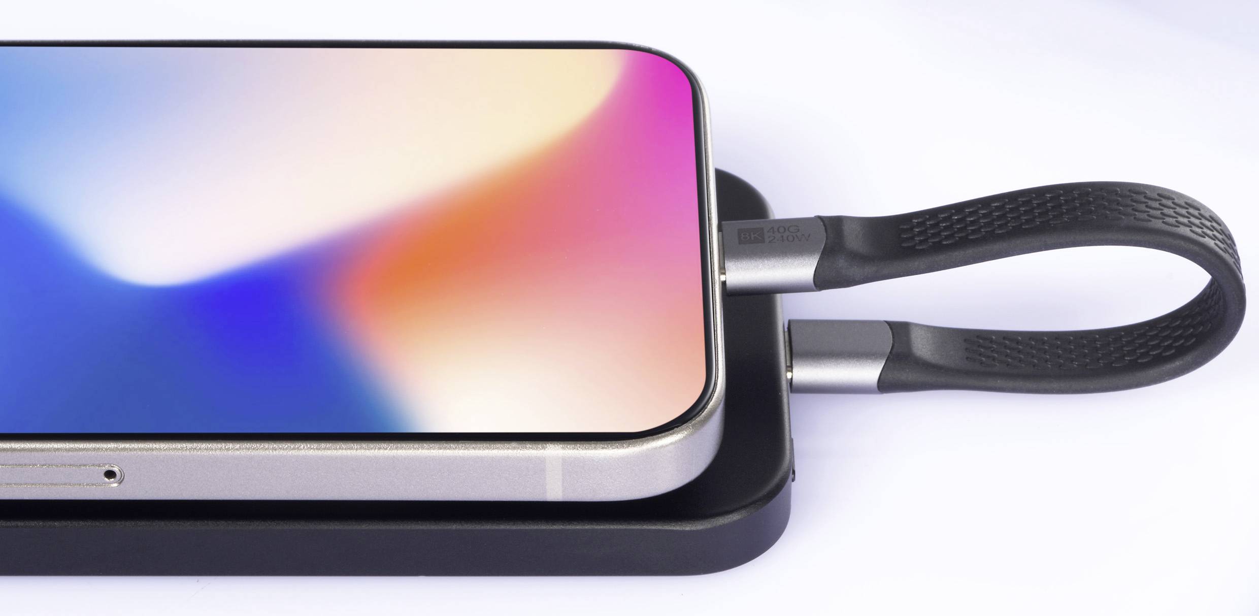 Ein Smartphone mit einem bunten Bildschirm ist über ein kurzes, schwarzes Kabel mit einem Ladegerät verbunden.