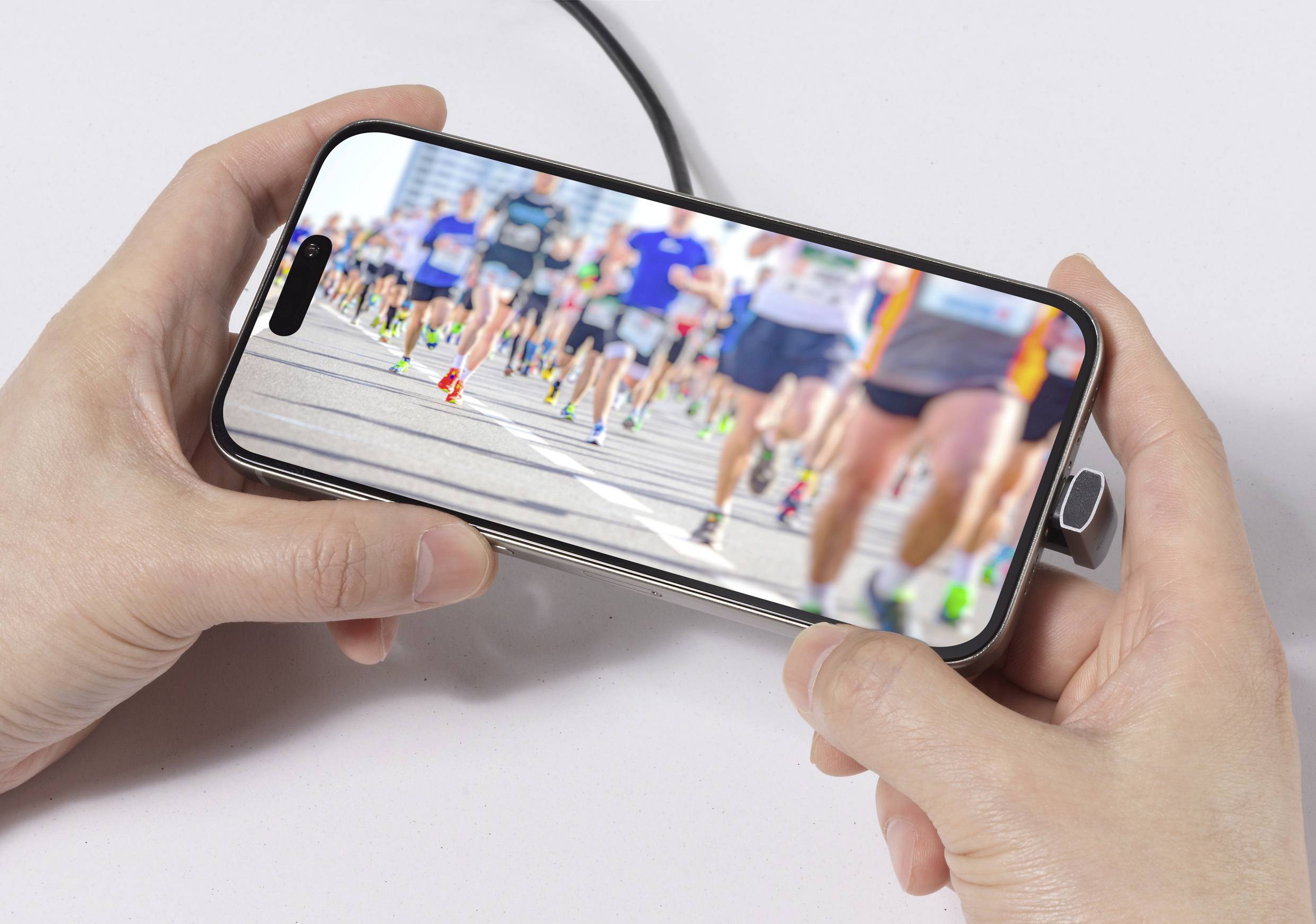 Hände, die ein Telefon halten, das ein verschwommenes Bild von Läufern bei einem Marathon zeigt, mit Fokus auf die Bewegung der Menge und die Vielfalt der Laufausrüstung.