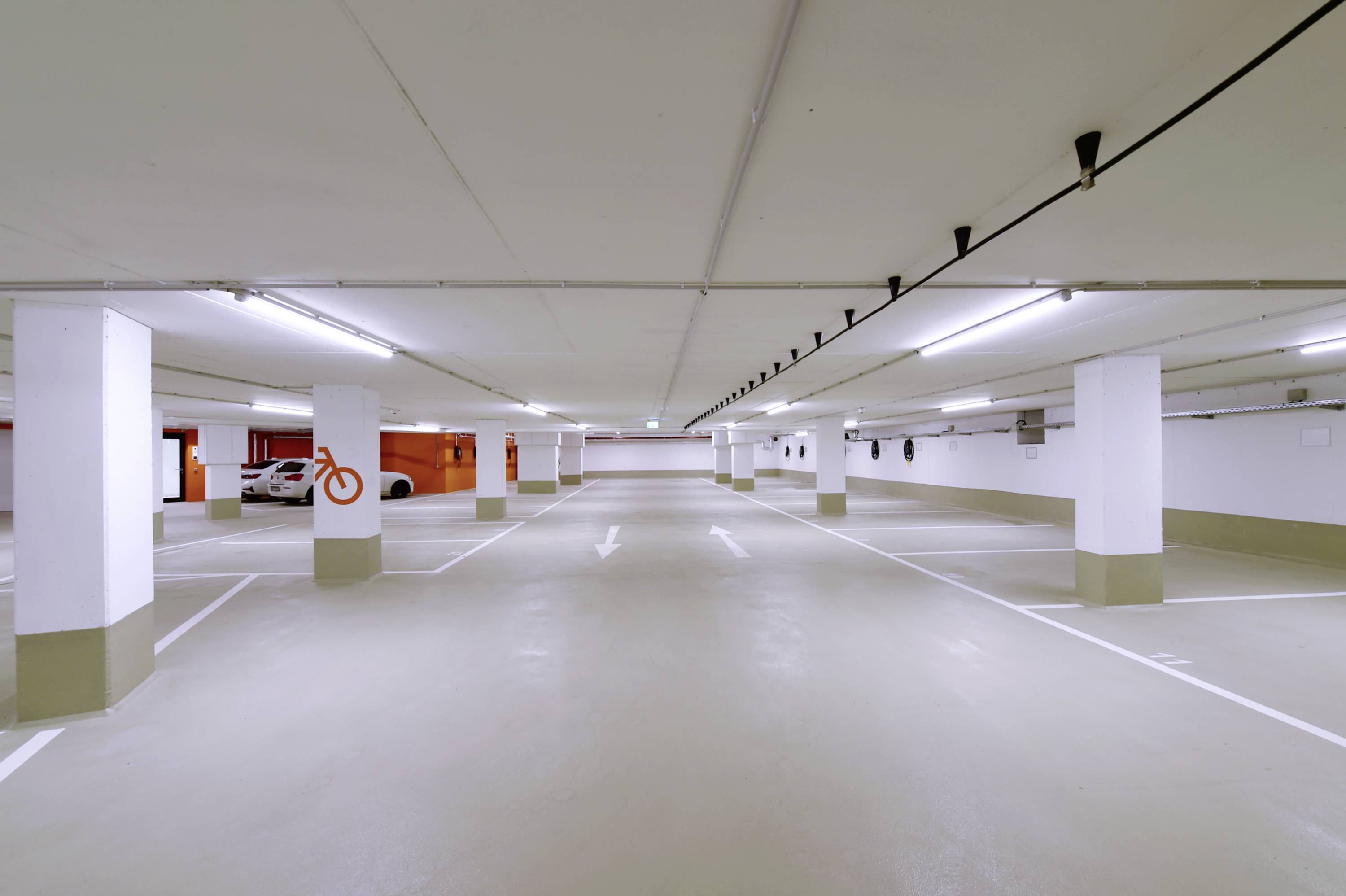 Ein leerer, hell beleuchteter Parkhausbereich mit weißen Markierungen auf dem Boden und Pfeilen, die die Fahrtrichtung anzeigen.