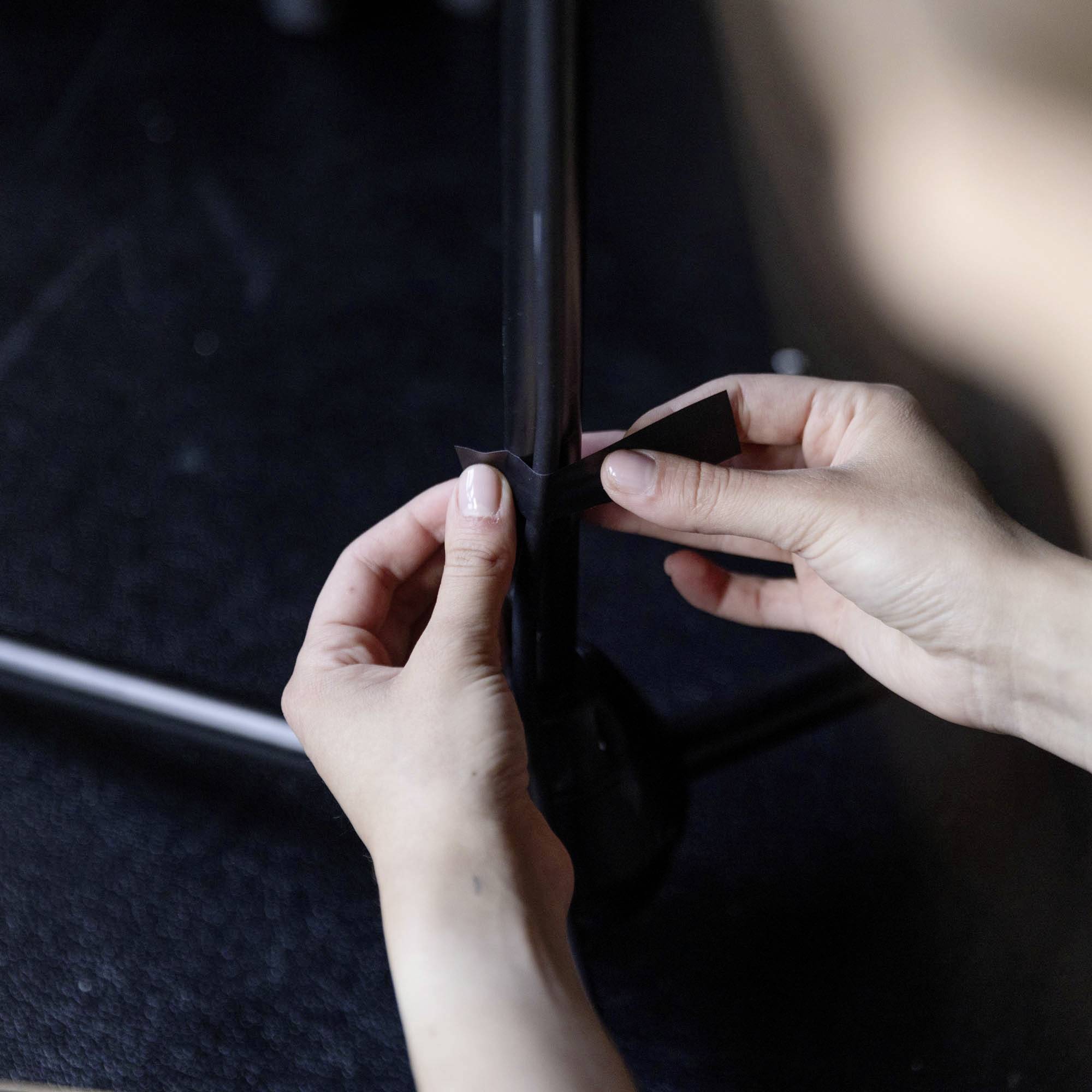 Eine Person klebt mit ihren Händen ein schwarzes Klebeband um ein Rohr.