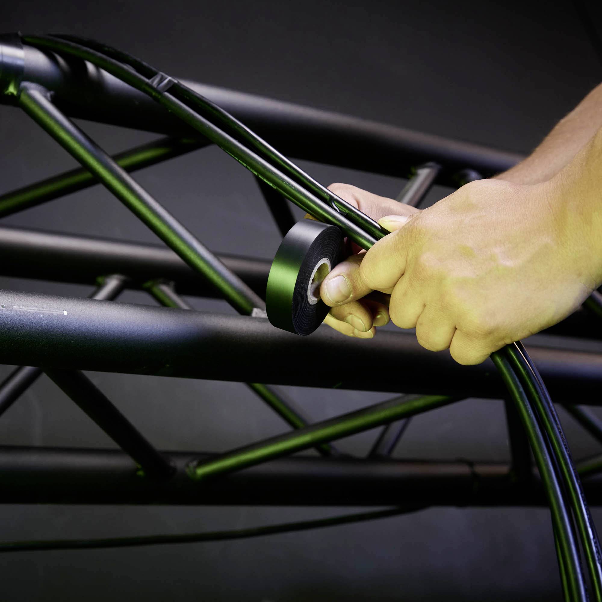 Nahaufnahme einer Hand, die schwarze Kabel mit Isolierband an einer schwarzen Metallstange fixiert.