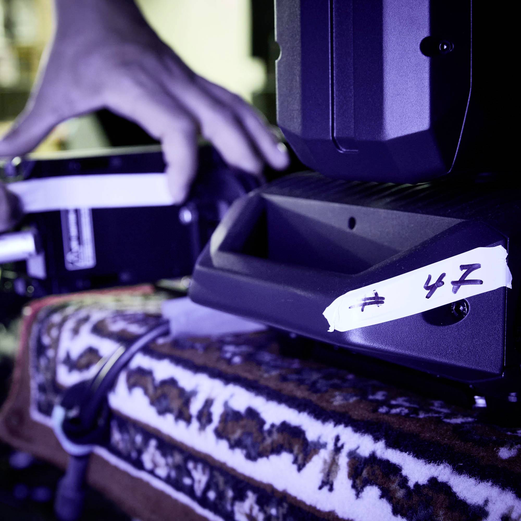 Personenhand justiert eine professionelle Kamera in einem Studio. Die Kamera ist auf einem gemusterten Stoff platziert.