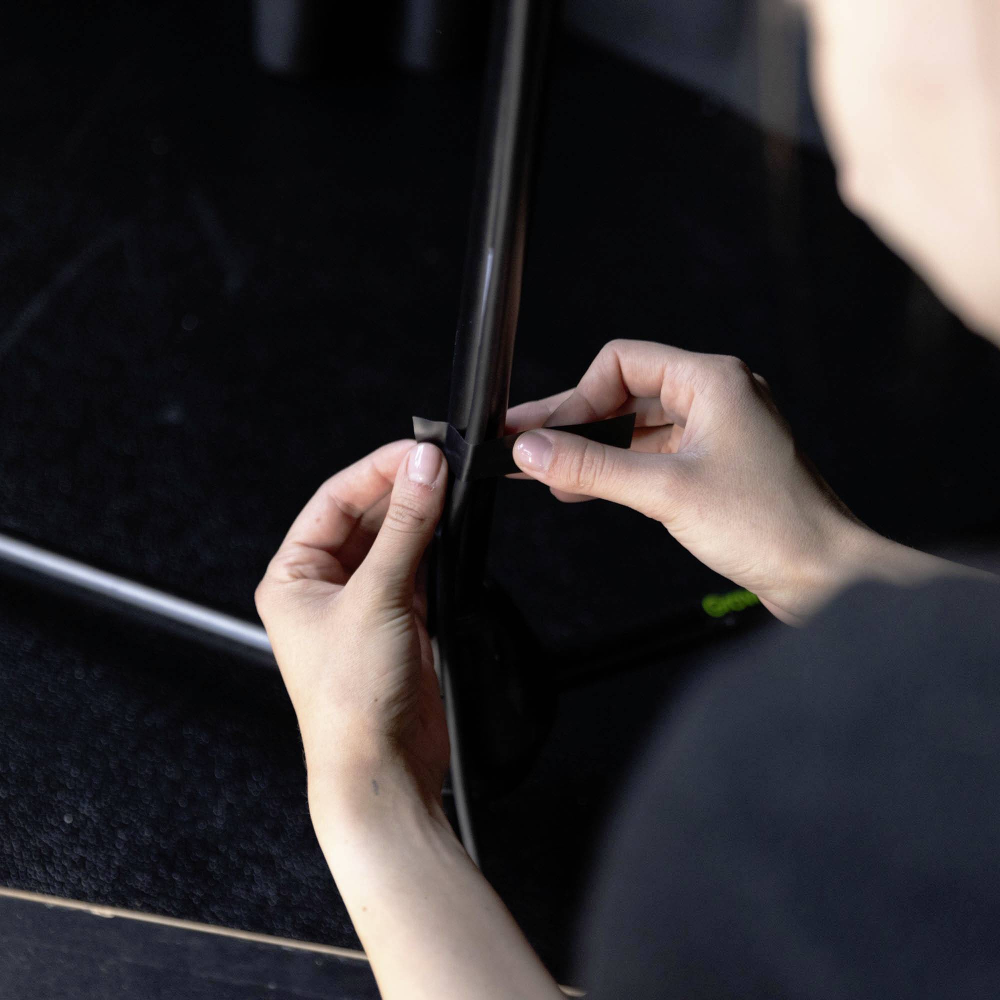 Eine Person klebt schwarzes Klebeband um einen Metallstab. Der Fokus liegt auf den Händen und dem Band.