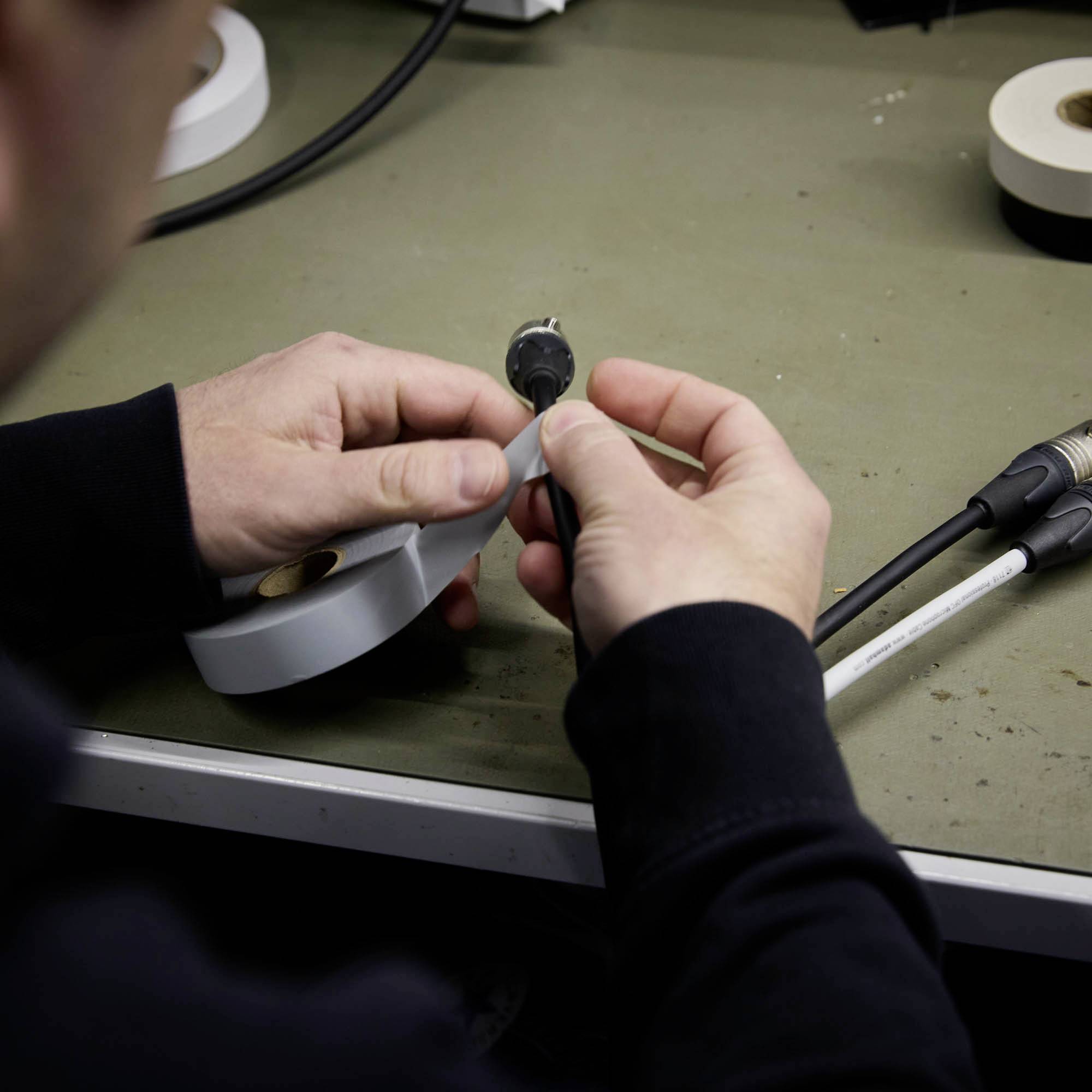 Eine Person hält ein Kabel und ein Verbindungsstück. Der Fokus liegt auf der Handhabung von Elektrokomponenten auf einem Tisch.