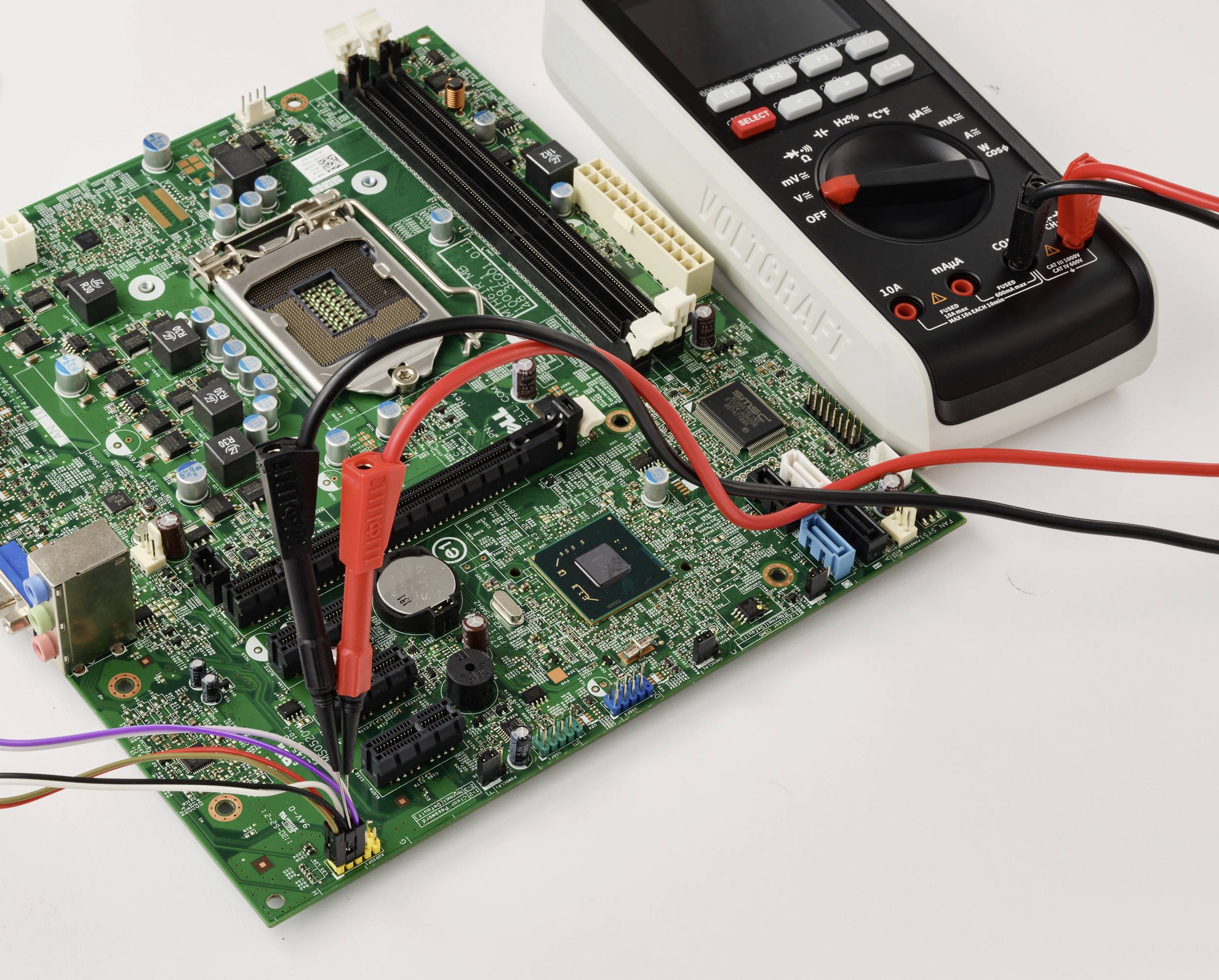 Ein digitales Multimeter mit roten und schwarzen Messspitzen ist an einer grünen Leiterplatte angeschlossen und misst Spannung oder Stromstärke.