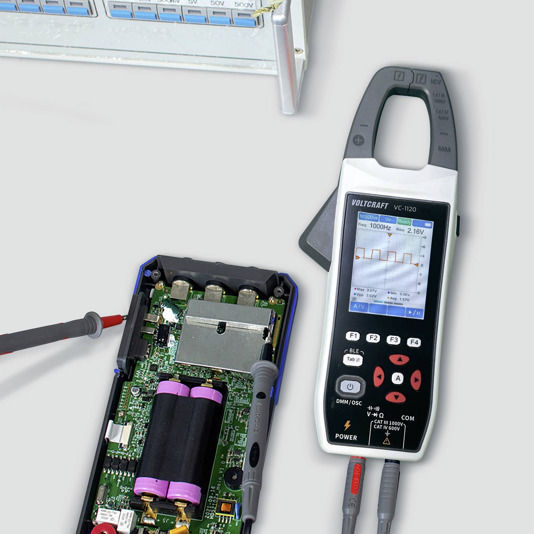 Ein digitales Multimeter, das die Spannung auf einer Leiterplatte mit Komponenten misst. Ein Gerät mit mehreren Anschlüssen ist im Hintergrund zu sehen.