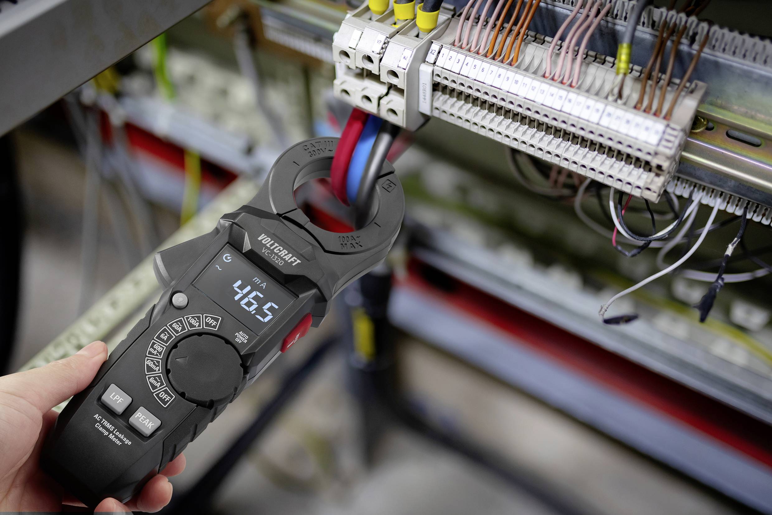 Eine Person verwendet ein digitales Zangenprüfgerät, um den elektrischen Strom in einem Stromkreis mit mehreren Drähten zu messen und zeigt einen Messwert von 46,5 an.