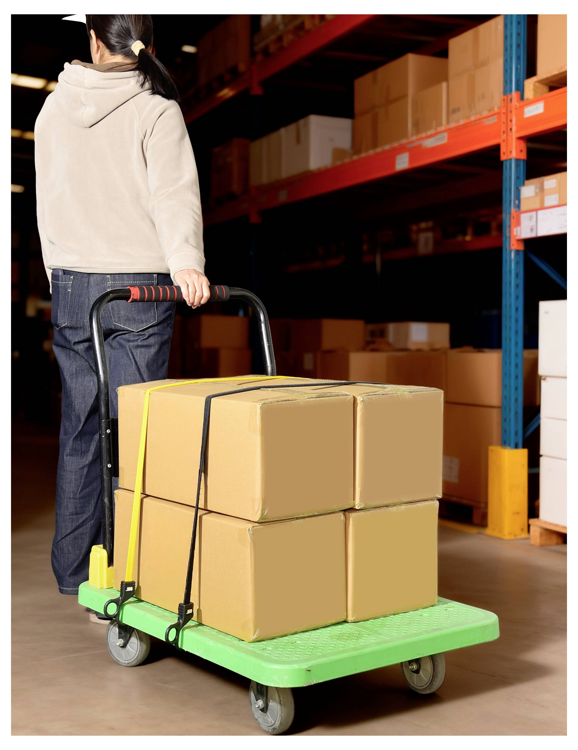 Person in Kapuzenpulli schiebt einen grünen Wagen mit sechs gestapelten Kartonschachteln in einem Lagergangs, umgeben von Regalen, die mit weiteren Kartons gefüllt sind.
