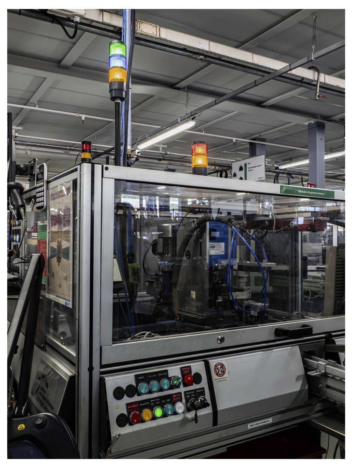 Automatisierte Industriemaschine auf einer Fertigungslinie mit blinkenden grünen, gelben und roten Statusleuchten sowie Bedienungstasten im Vordergrund.