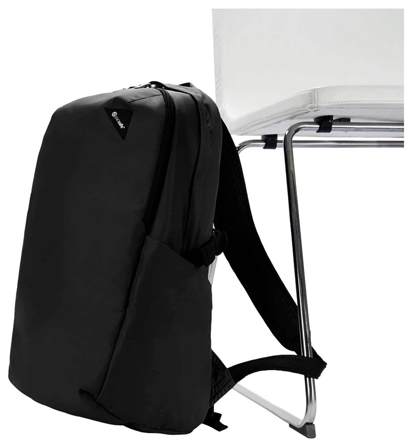 Ein schwarzer Rucksack steht aufrecht auf einem weißen Stuhl und präsentiert sein schlankes Design mit sichtbarem Markenlogo in der Nähe des oberen Randes.