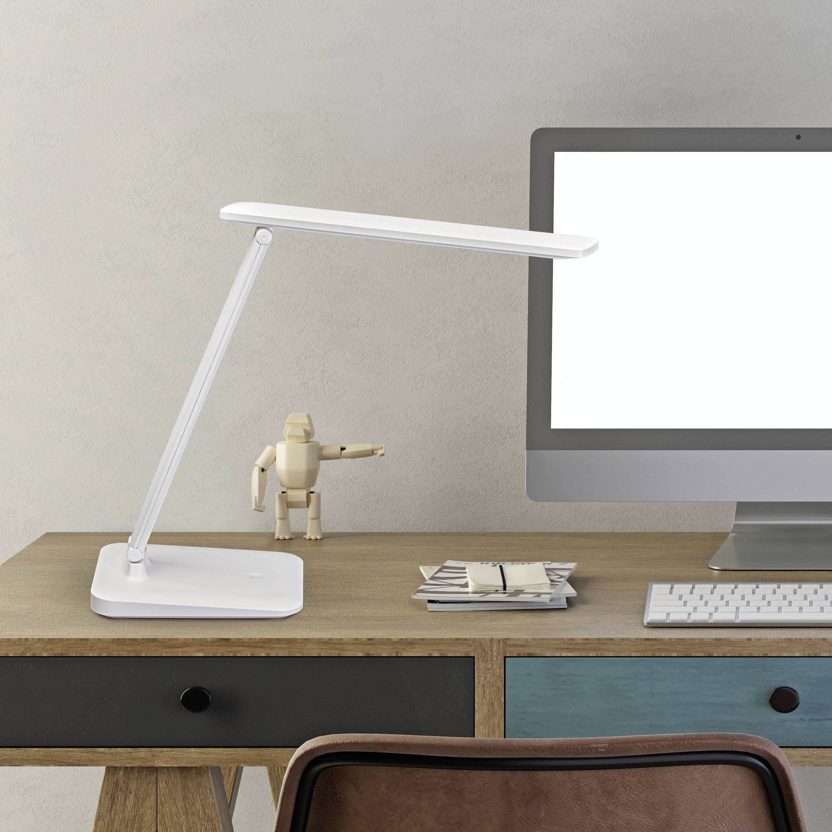 Ein moderner Arbeitsplatz mit einer eleganten Schreibtischlampe, einem Desktop-Computer mit leerem Bildschirm, einem kleinen Stapel Papiere und einer Figur auf einem Holzschreibtisch.