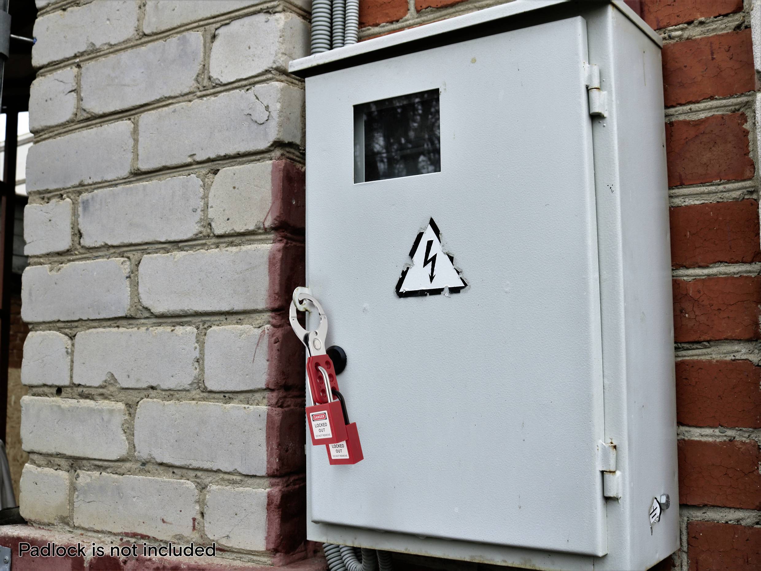 Metallische Elektroverteilerdose mit einem Blitzsymbol an einer Ziegelwand, versiegelt mit einem roten Sicherheitsverriegelungsetikett. Warnhinweis: Vorhängeschloss nicht im Lieferumfang enthalten.'