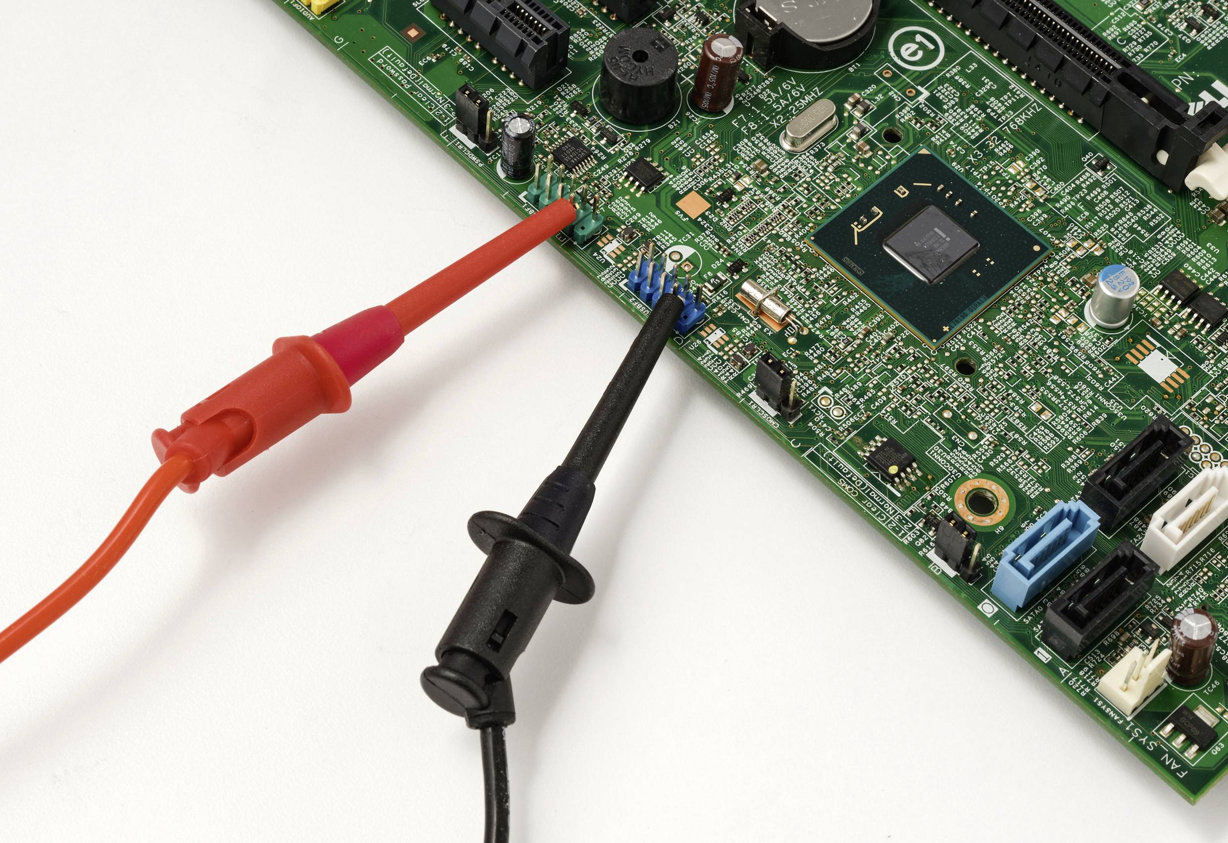 Zwei Multimeter-Messspitzen in Rot und Schwarz testen eine Leiterplatte, die dicht mit elektronischen Komponenten bestückt ist und dabei eine diagnostische Analyse hervorheben.