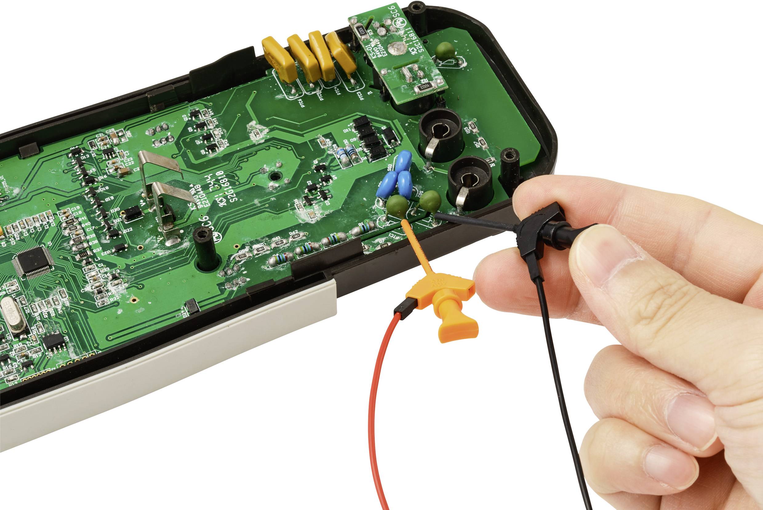 Eine Hand hält Messsonden auf einer Leiterplatte. Die Leiterplatte ist grün mit verschiedenen elektronischen Bauteilen. Der Zweck deutet auf Tests oder Reparatur hin.