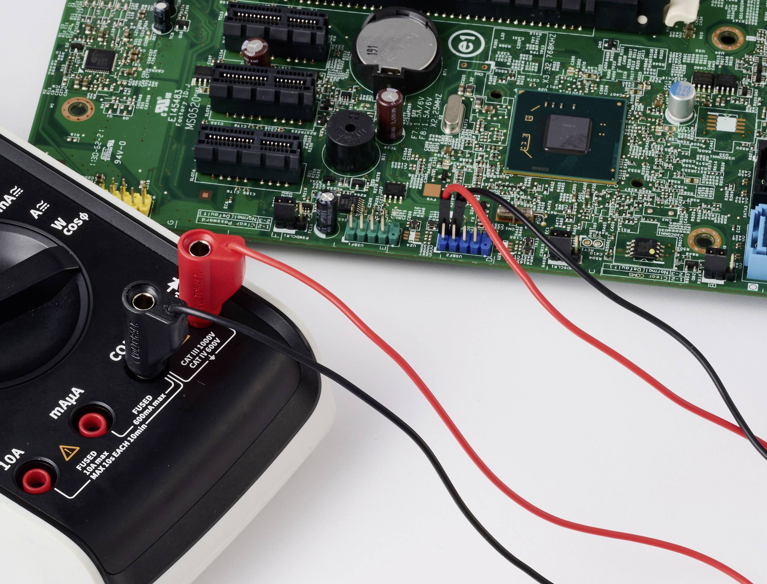 Ein digitales Multimeter mit Messspitzen ist an einer grünen Leiterplatte zur Prüfung elektronischer Bauteile angeschlossen.