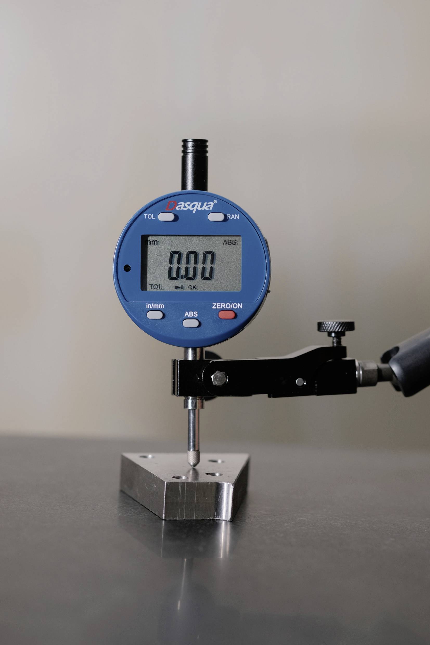 Digitaler Messschieber, der einen kleinen Metallblock auf einer ebenen Oberfläche misst und '0,00' auf dem Display zeigt, was keine Abweichung anzeigt.
