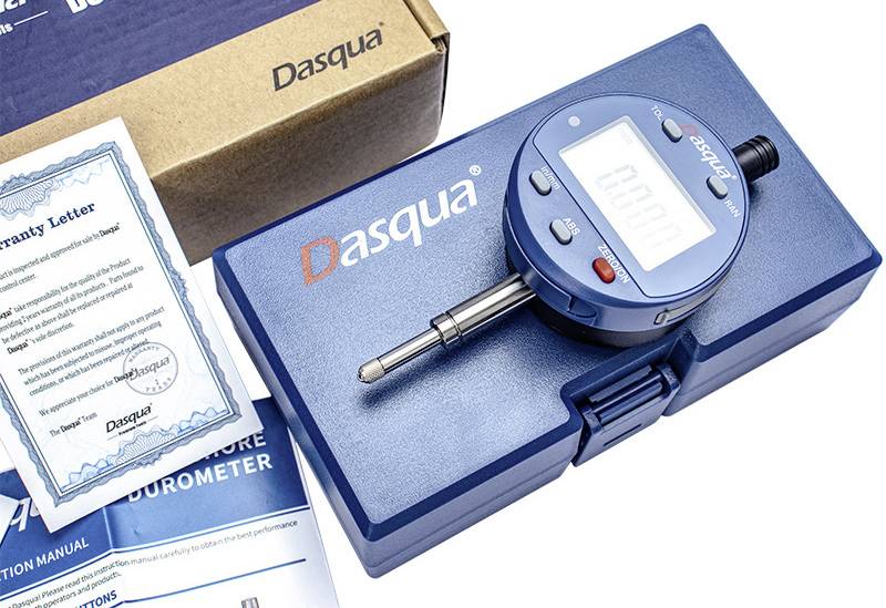 Ein digitales Durometer-Messgerät auf einem blauen Gehäuse mit dem 'Dasqua' Logo, neben Bedienungsanleitungen und einem Garantieschreiben, was auf Kalibrierwerkzeuge hinweist.