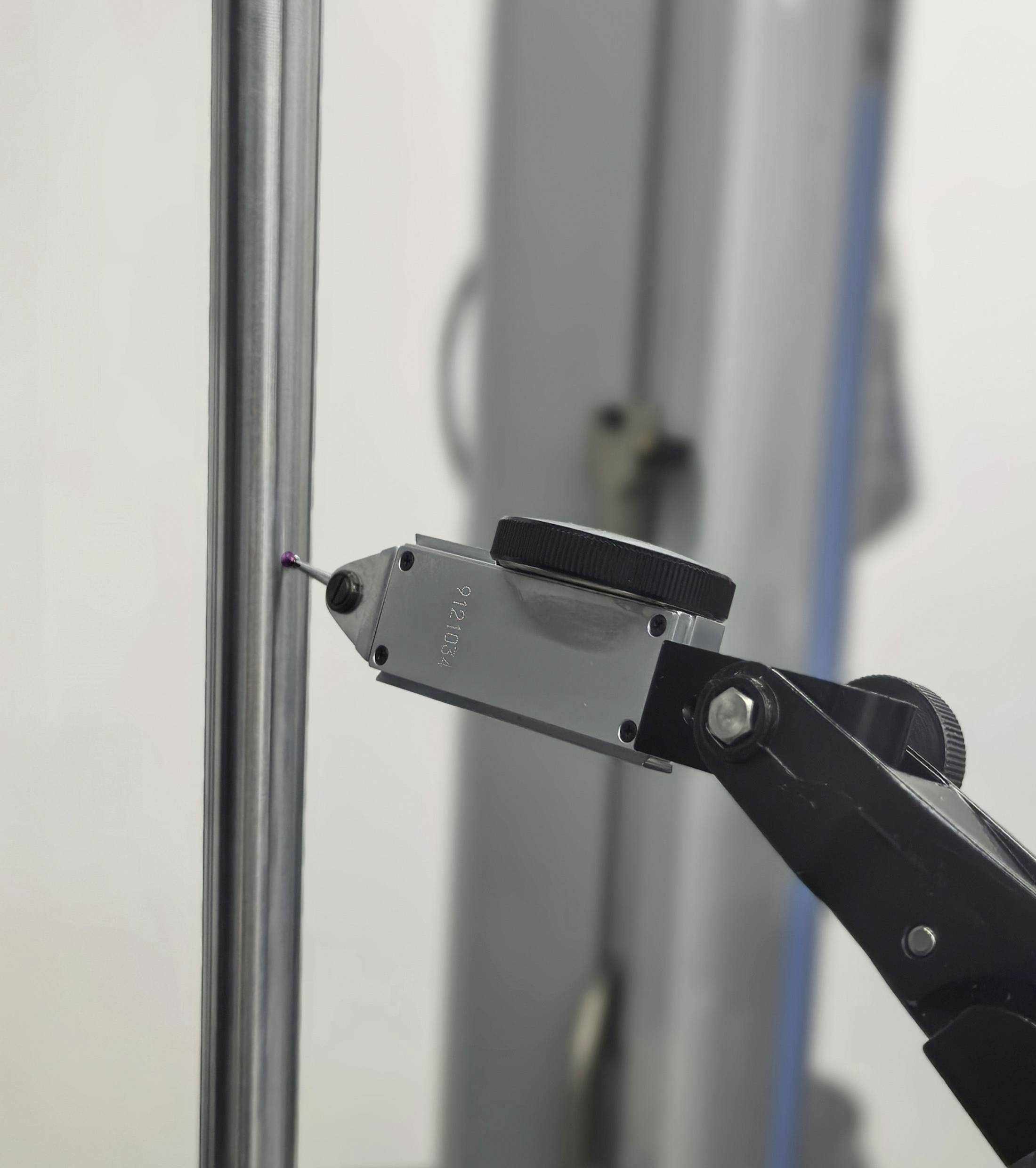 Ein Präzisionsmessgerät mit digitalem Messanzeiger berührt einen Metallstab, wahrscheinlich im Rahmen eines Test- oder Kalibrierungsprozesses.