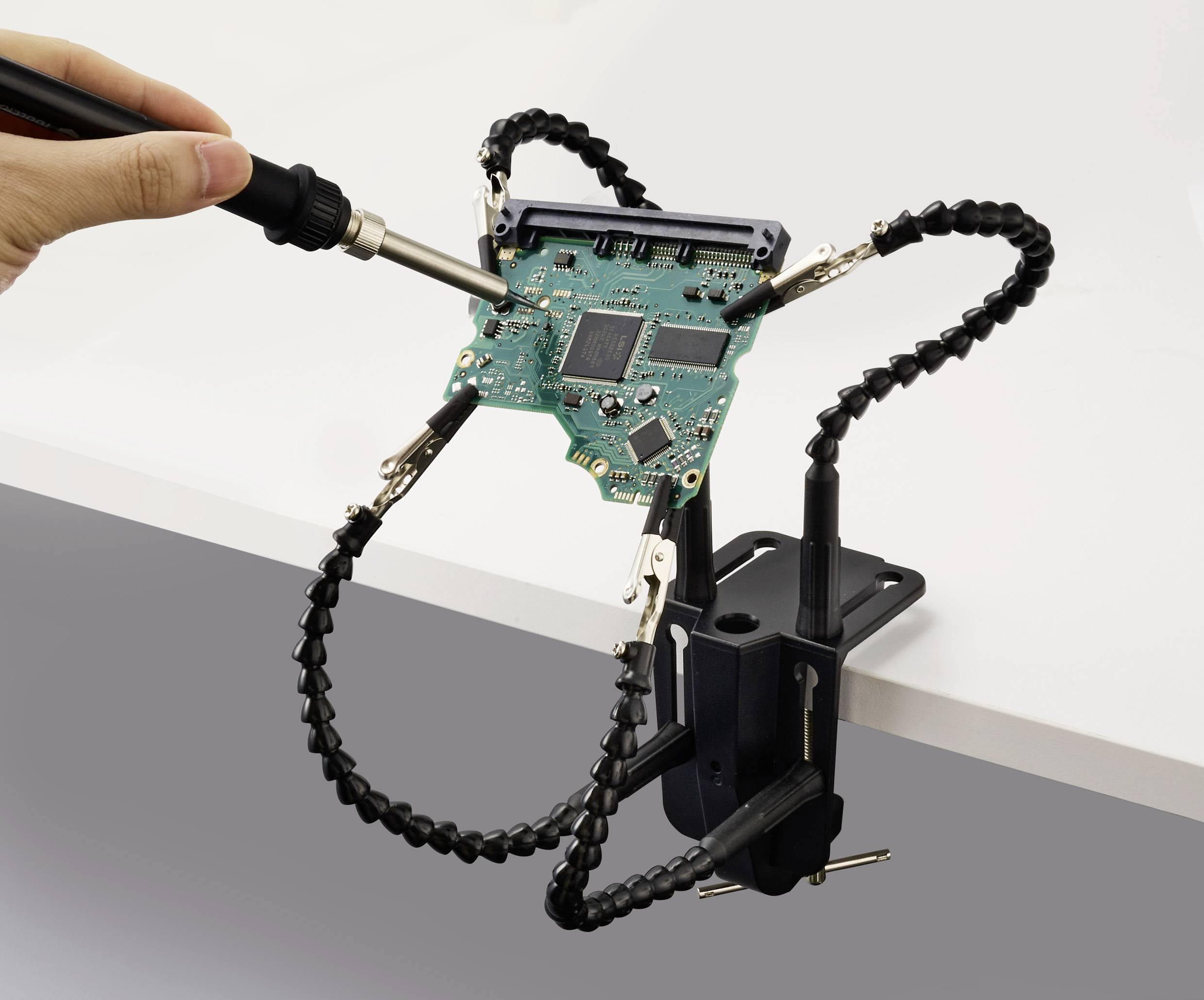 Eine Hand einer Person lötet eine Computerplatine, die in einer flexiblen Armklemme befestigt ist und damit Elektronik-Reparatur oder -Montage demonstriert.