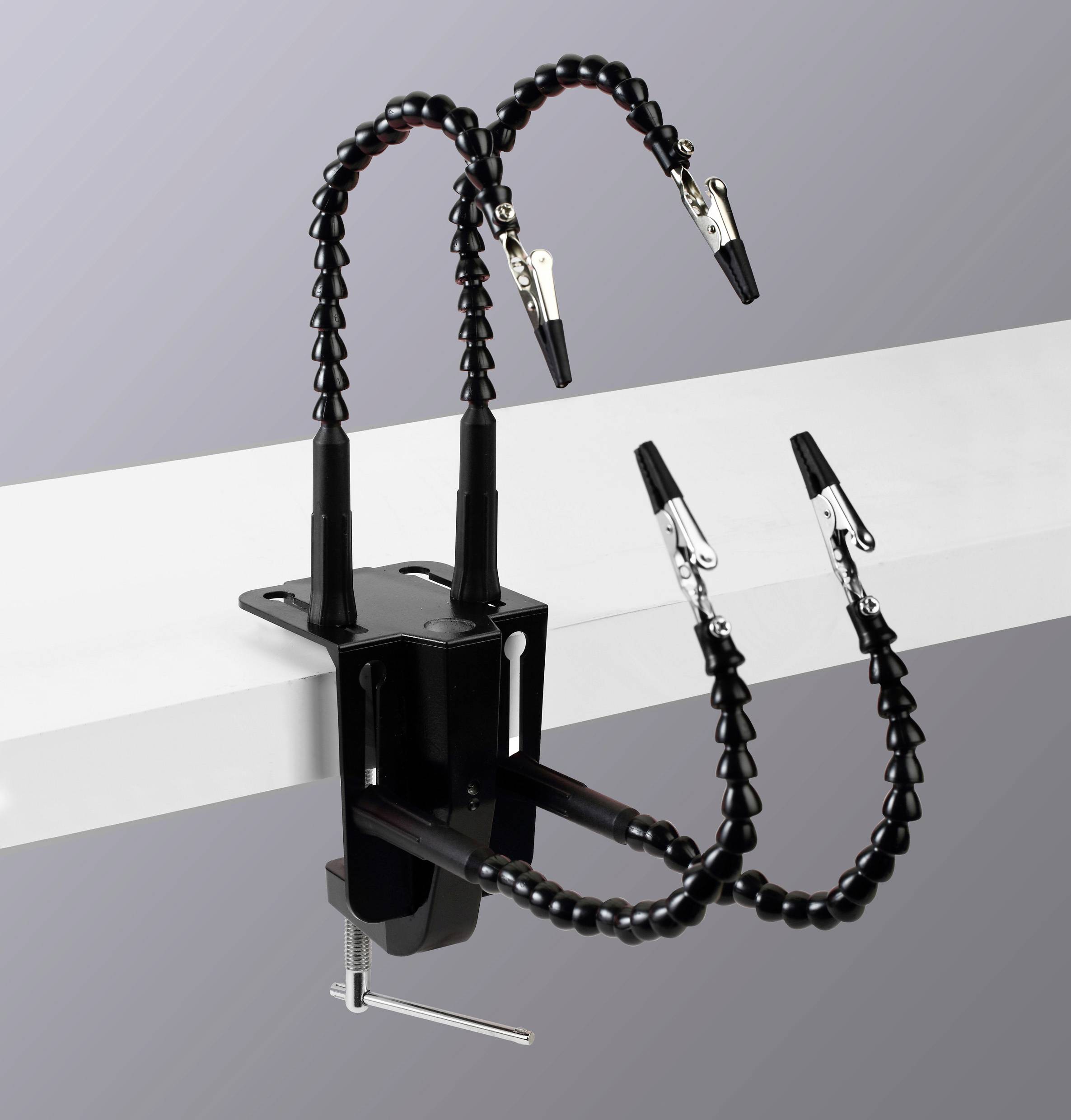 Eine flexible Klammer mit vier Krokodilklemmen an verstellbaren Armen, die an einer flachen Oberfläche befestigt ist und zum Sichern von Objekten während der Montage oder Reparatur verwendet wird.