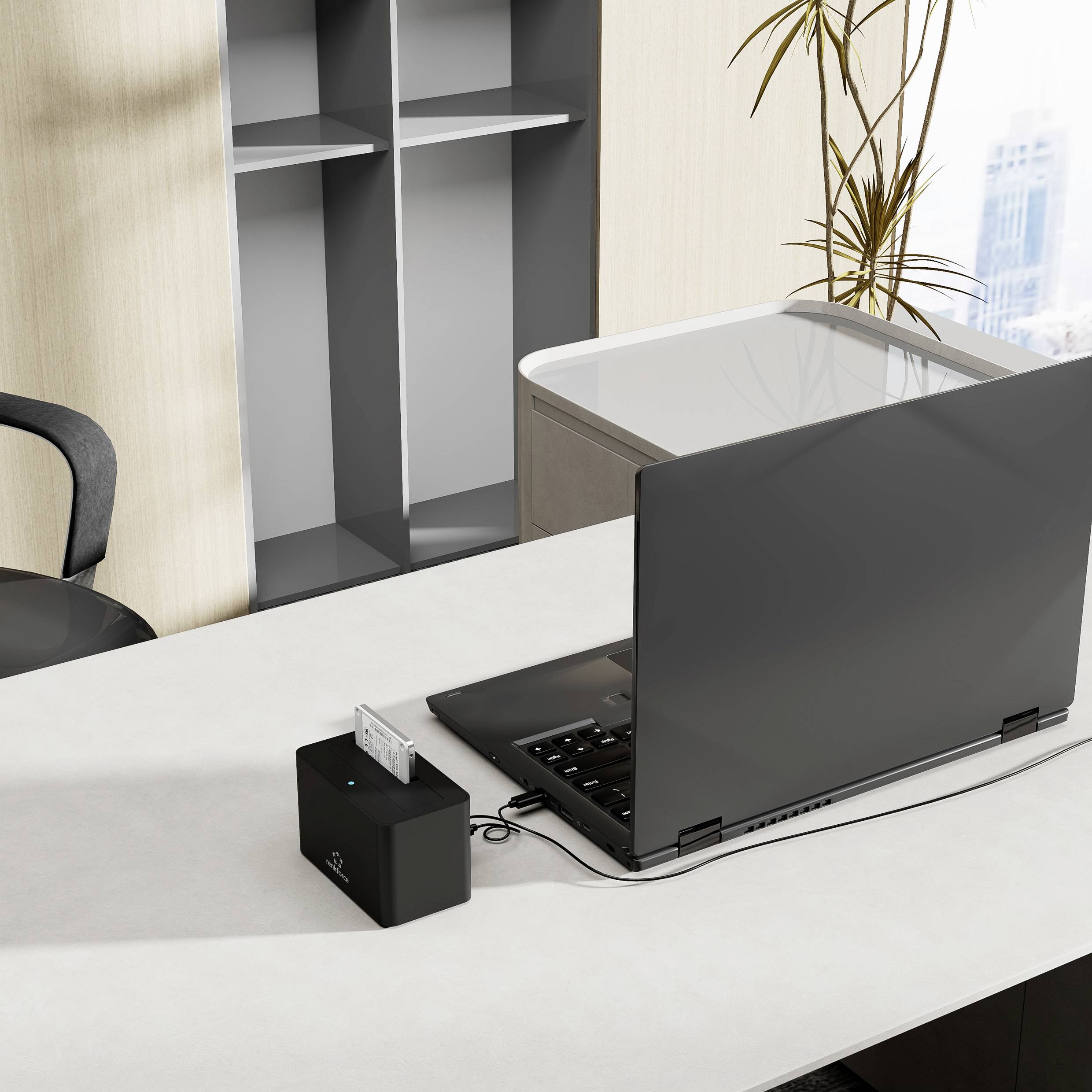 Ein moderner Büroschreibtisch mit einem offenen Laptop, einem Stuhl, einer kleinen Pflanze und einem Organizer mit leeren Regalen im Hintergrund.