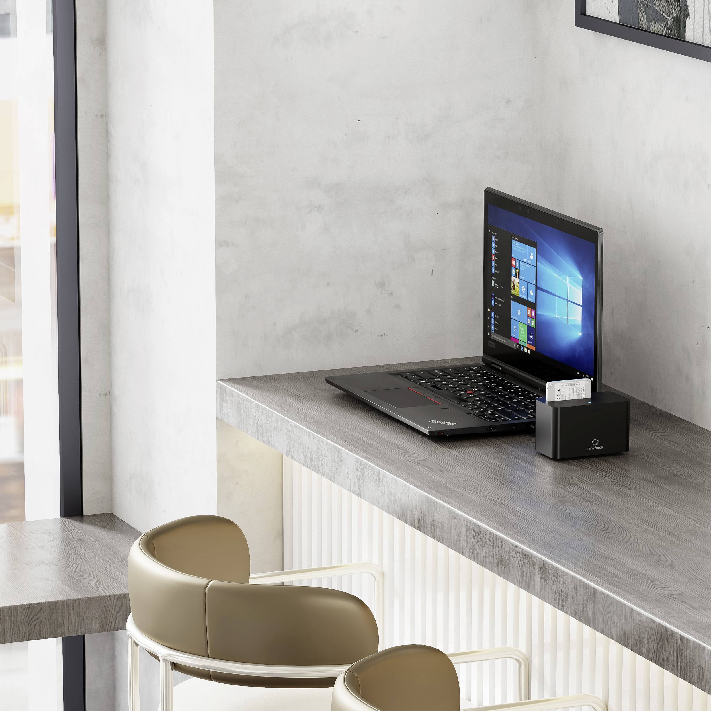 Eine moderne Büroarbeitsplatz-Einrichtung mit einem geöffneten Laptop, auf dem Windows angezeigt wird, einem Kartenständer und zwei beigen Stühlen vor einem großen Fenster.