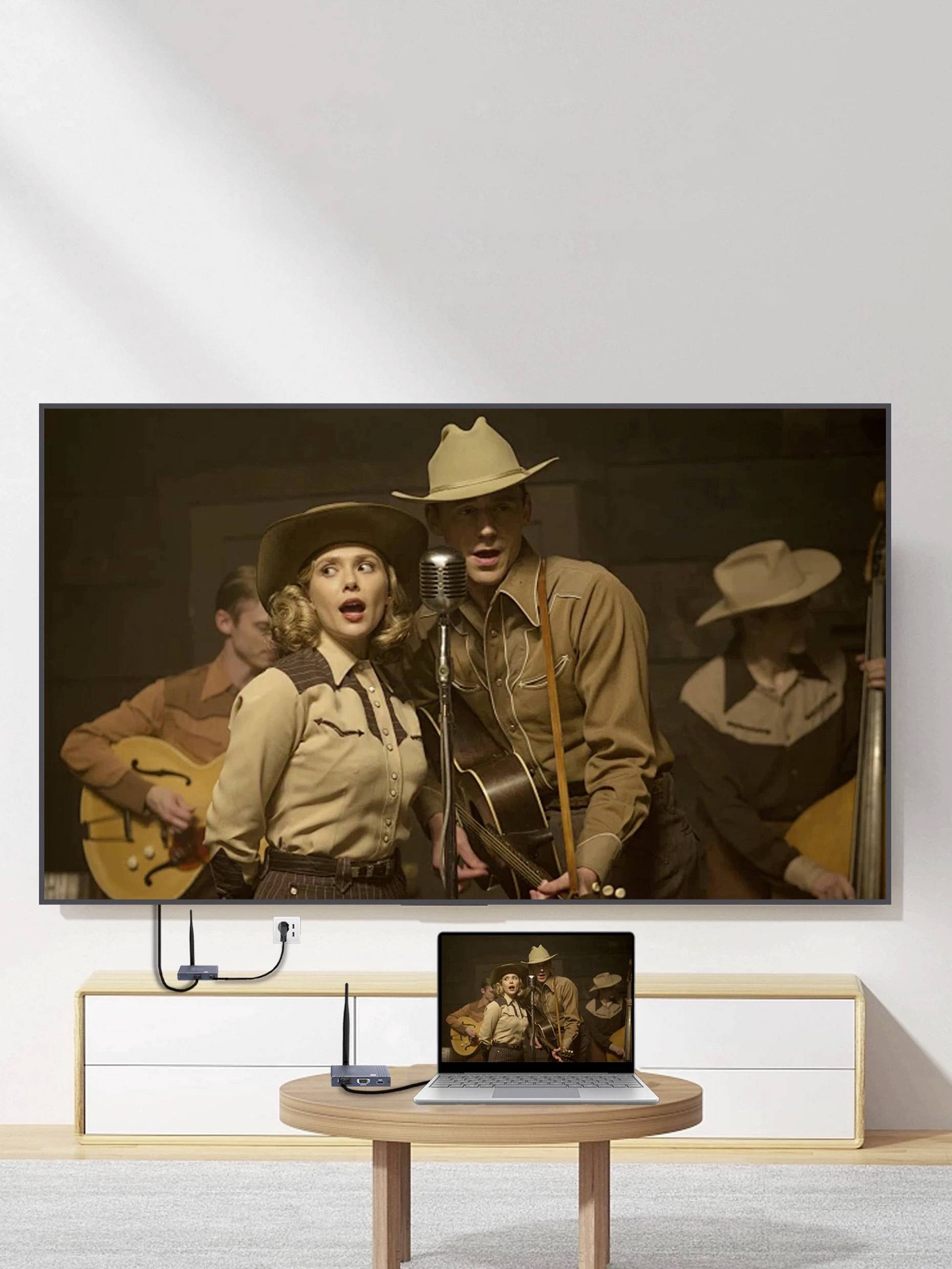 Eine Wohnzimmereinrichtung mit einem Fernseher und einem Laptop, die eine Szene mit zwei Personen in Cowboy-Kleidung zeigen, die mit einer Band auftreten.