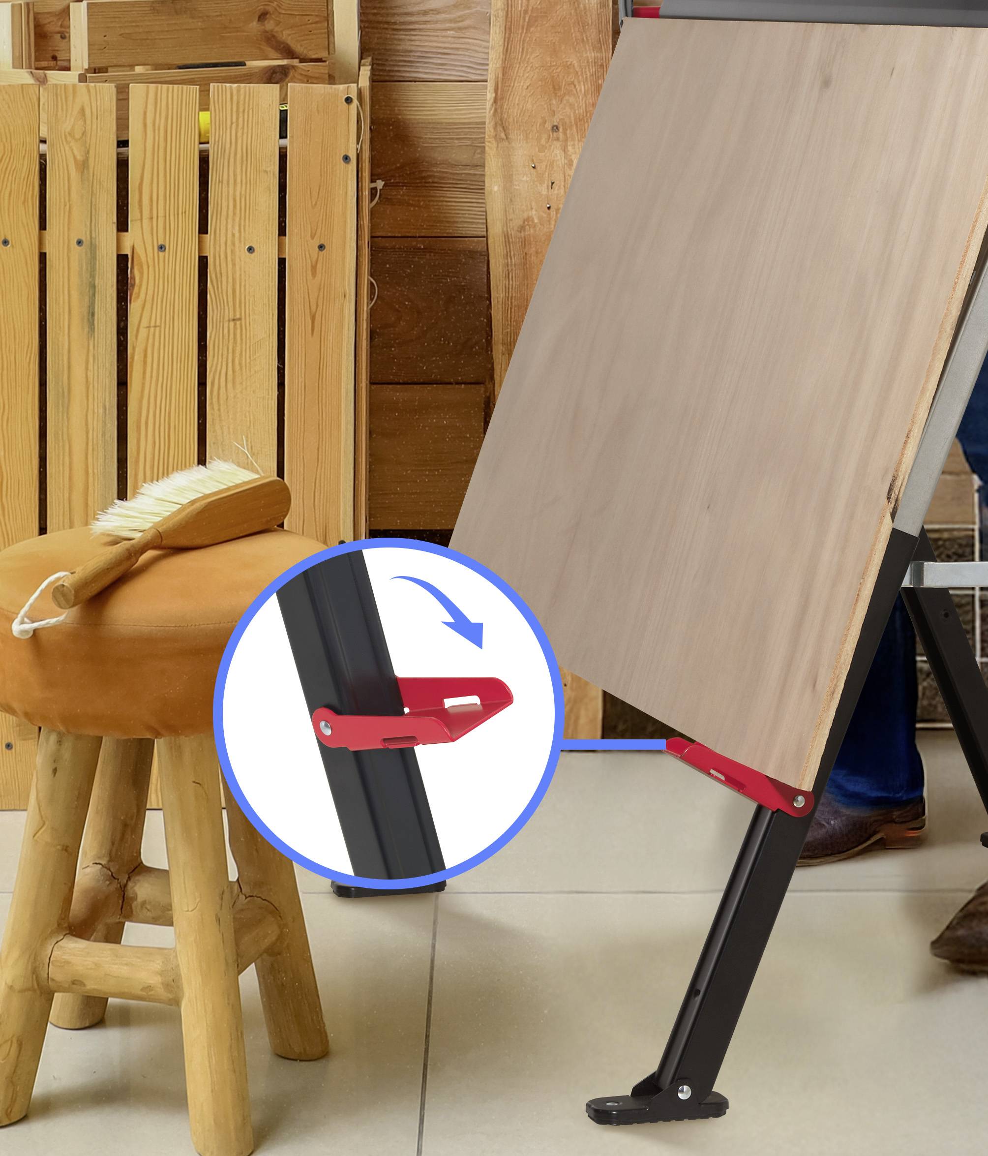 Verstellbare Staffelei mit rotem Verschlussmechanismus, positioniert neben einem Holzhocker, auf dem ein Pinsel liegt. Holztafel im Hintergrund.