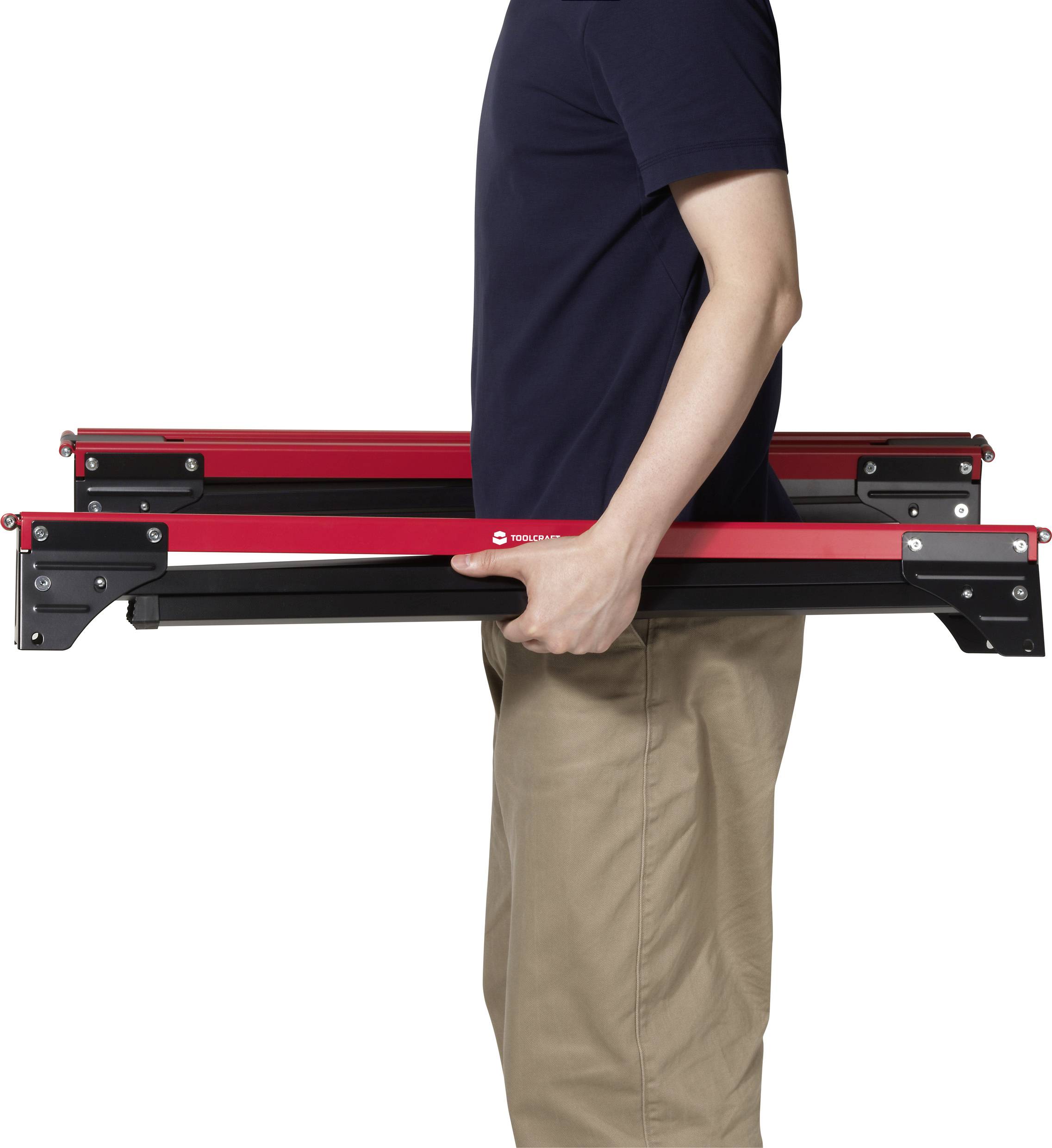 Eine Person in einem marineblauen Hemd und khakifarbenen Hosen trägt eine kompakte, zusammengefaltete rot-schwarze Leiter horizontal auf Hüfthöhe.